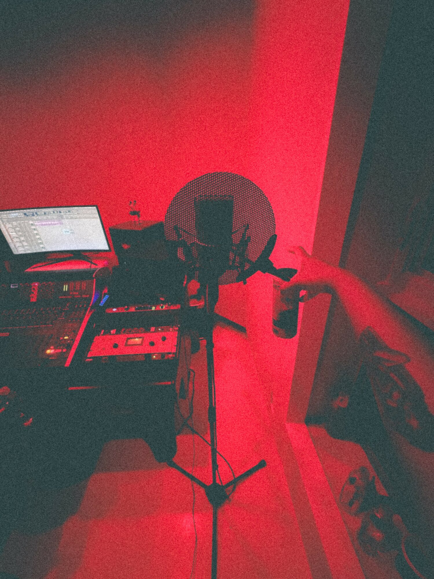 DJ equipment setup with a laptop, speakers, and a hand adjusting controls in a red-lit room.