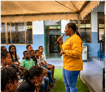 Woman speaking into microphone to children seated outdoors under a canopy, with blue building in background.
