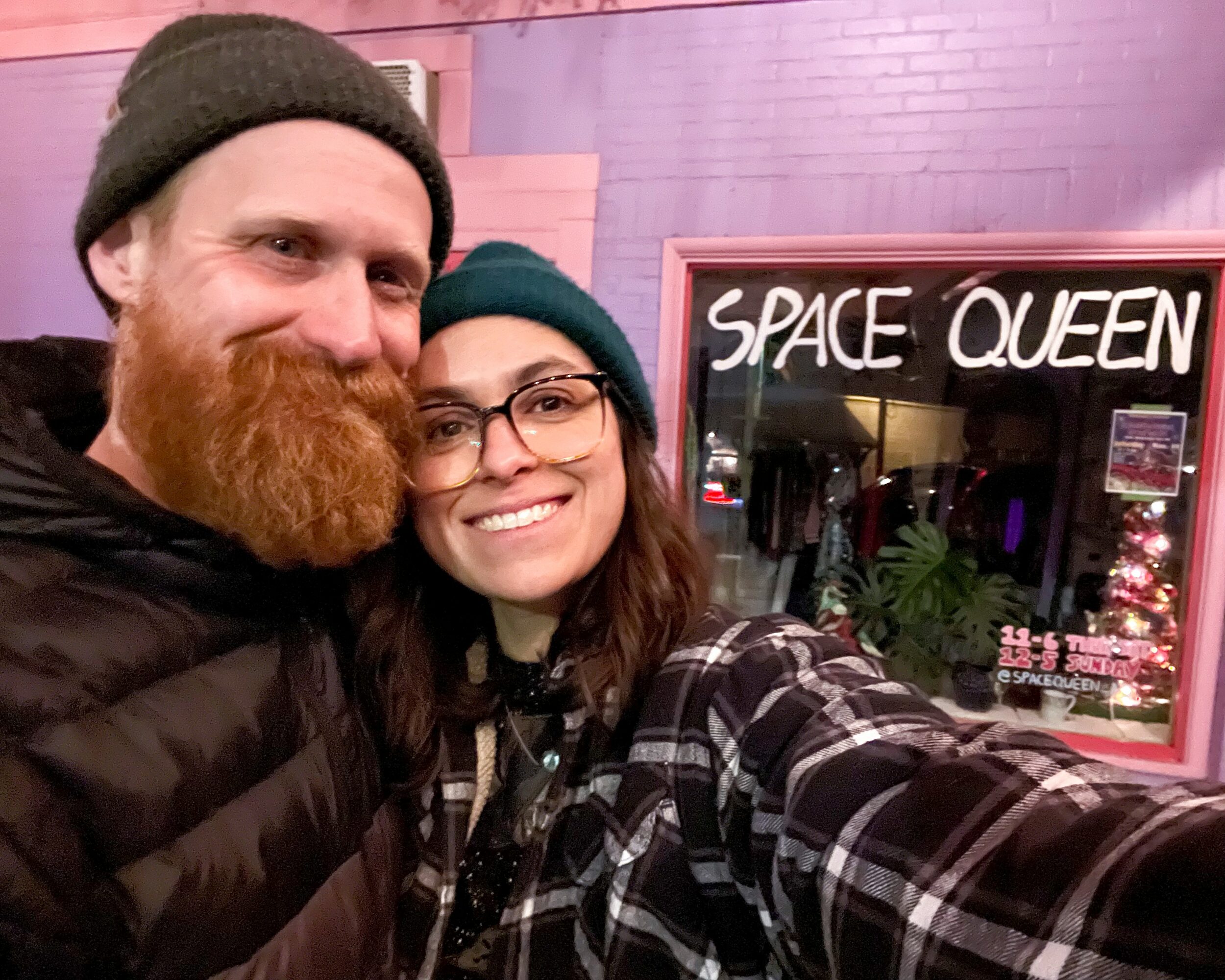 Two people smiling in front of a store with a sign that reads 'SPACE QUEEN'.
