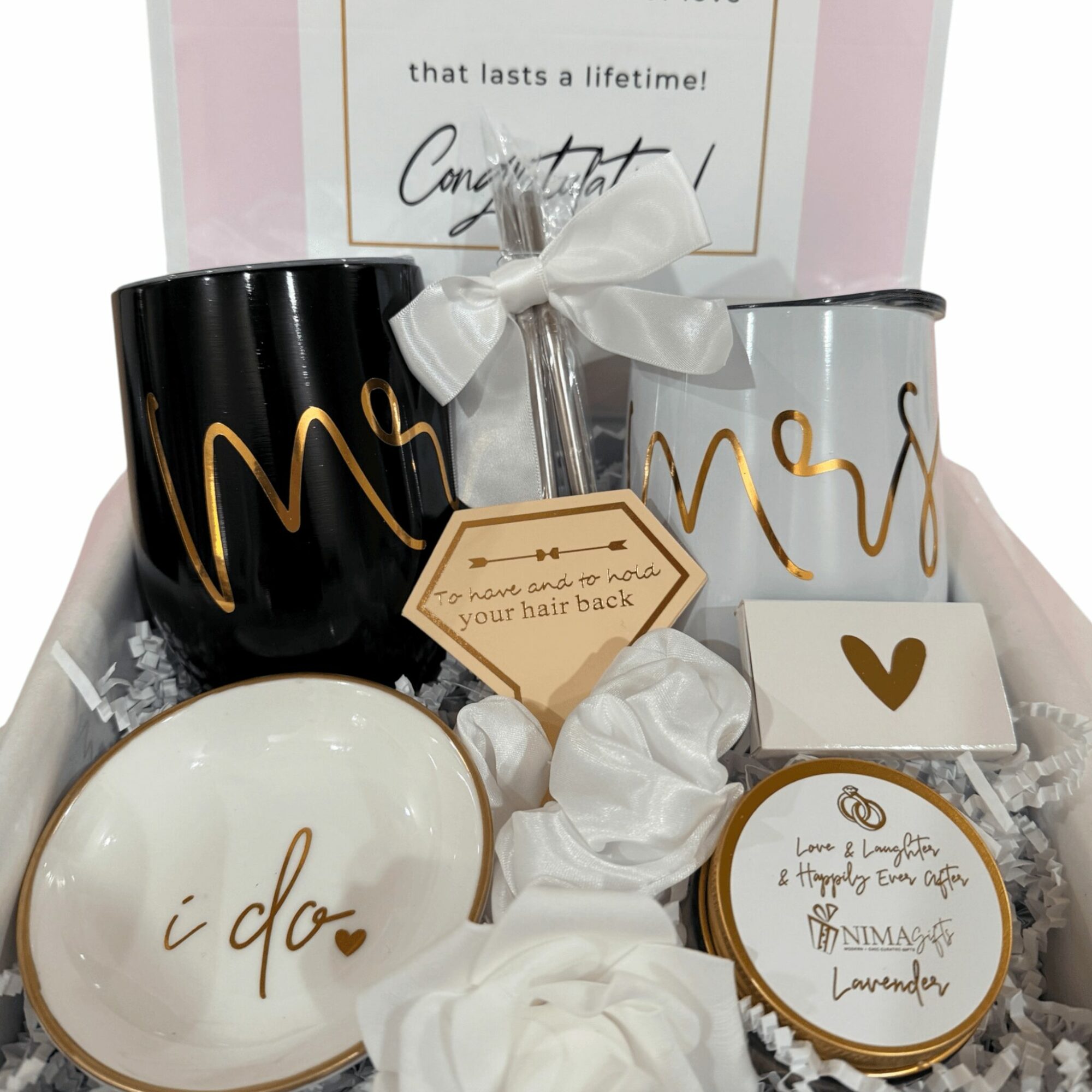 Two mugs, a small plate, and a jar with gold writing, surrounded by tissue paper and a gift card, in a gift box.