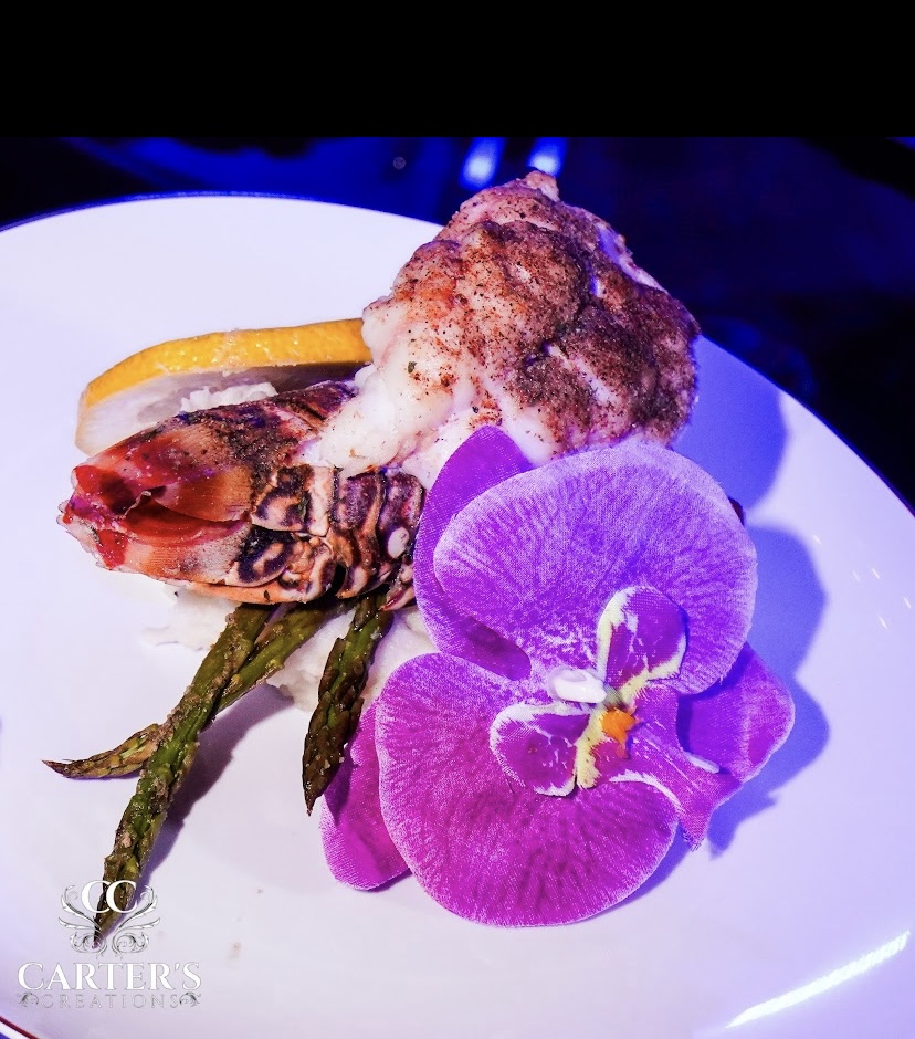 Plate with grilled vegetables, a fried item topped with sauce, and a purple orchid flower, on a white dish.
