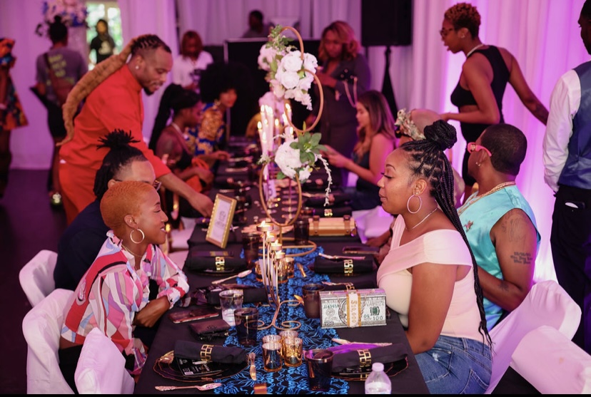 People gathered around a decorated table with flowers and candles at an indoor event, pink lighting in the background.