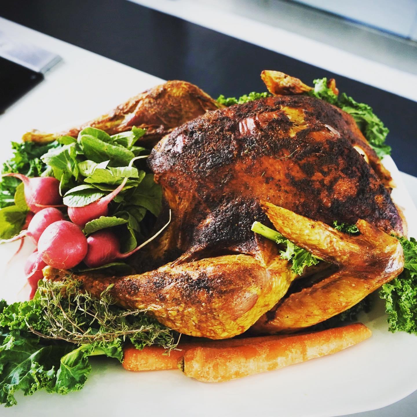 Roast chicken with radishes, carrots, and leafy greens on a white plate.