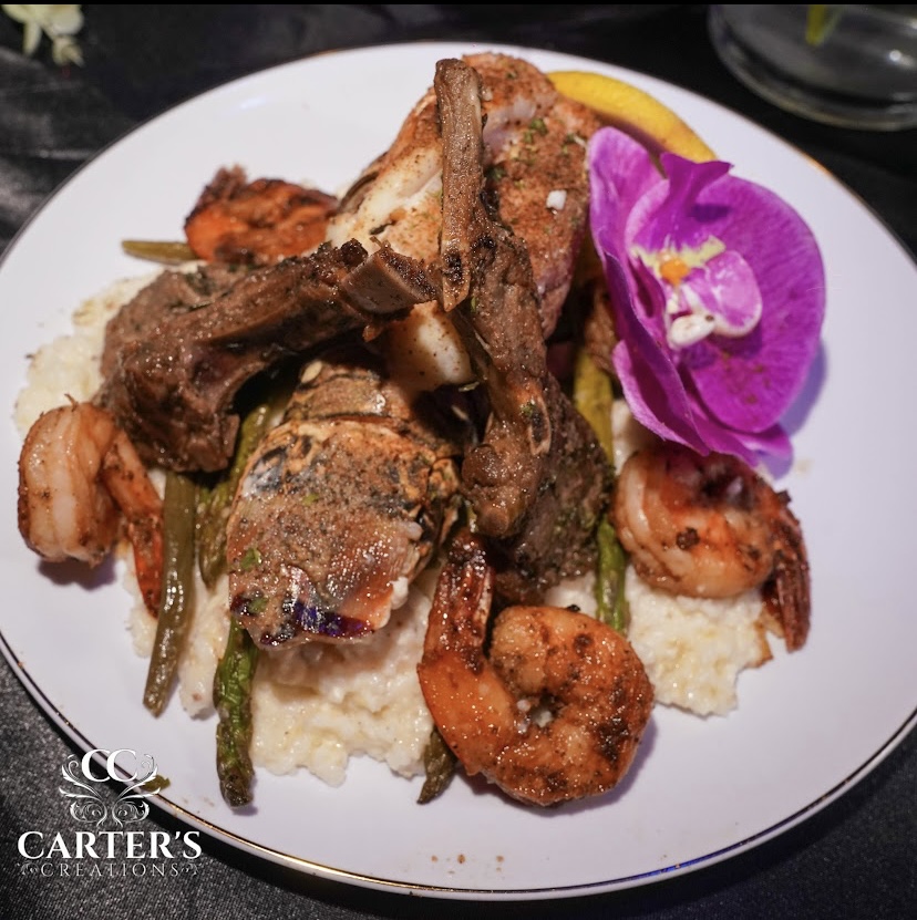 Plate with lamb chops, shrimp, mashed potatoes, green beans, and a purple orchid flower garnish.