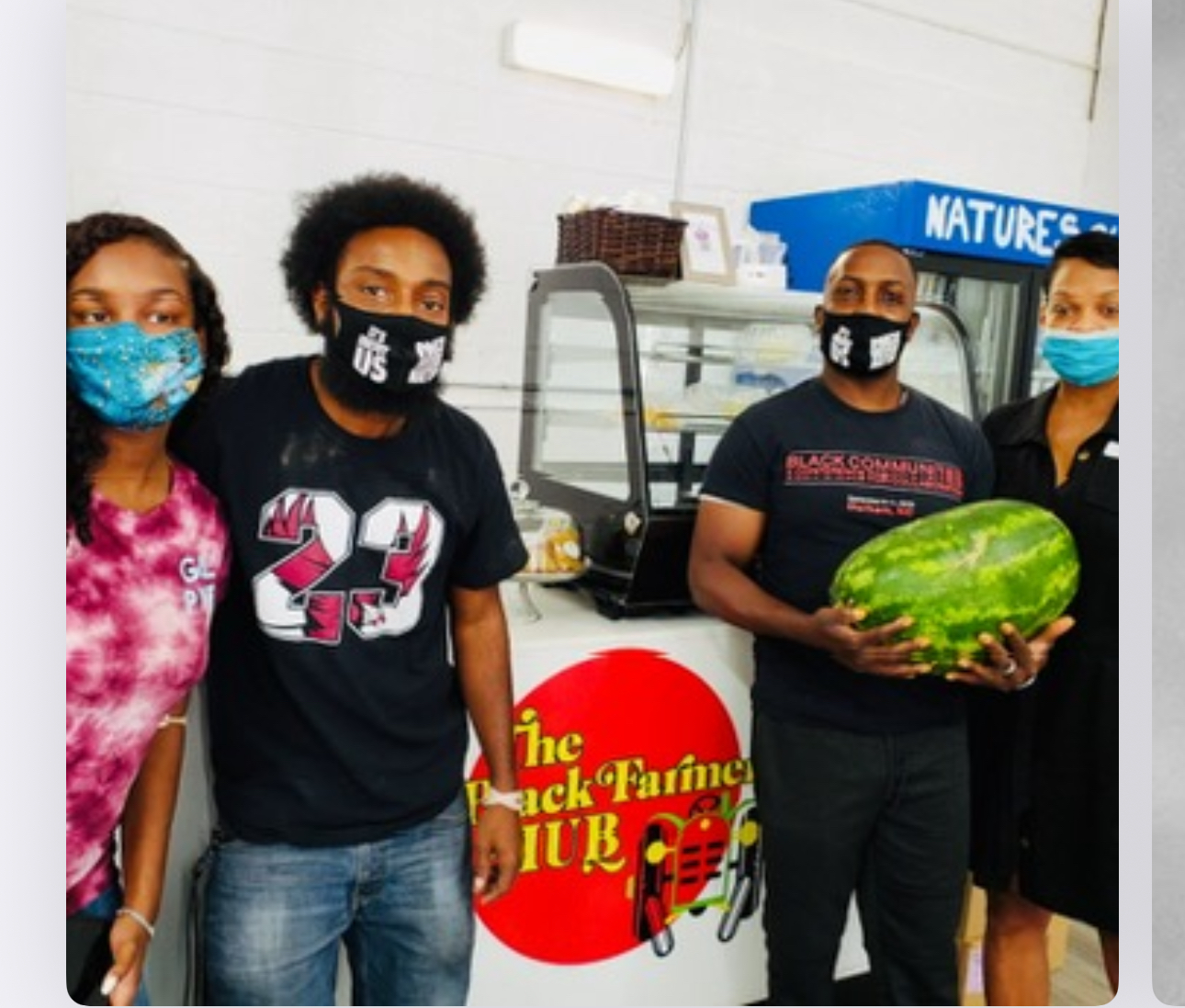 Four people standing in front of a display case, one holding a watermelon, with a sign reading 'The Black Farmers Club'.