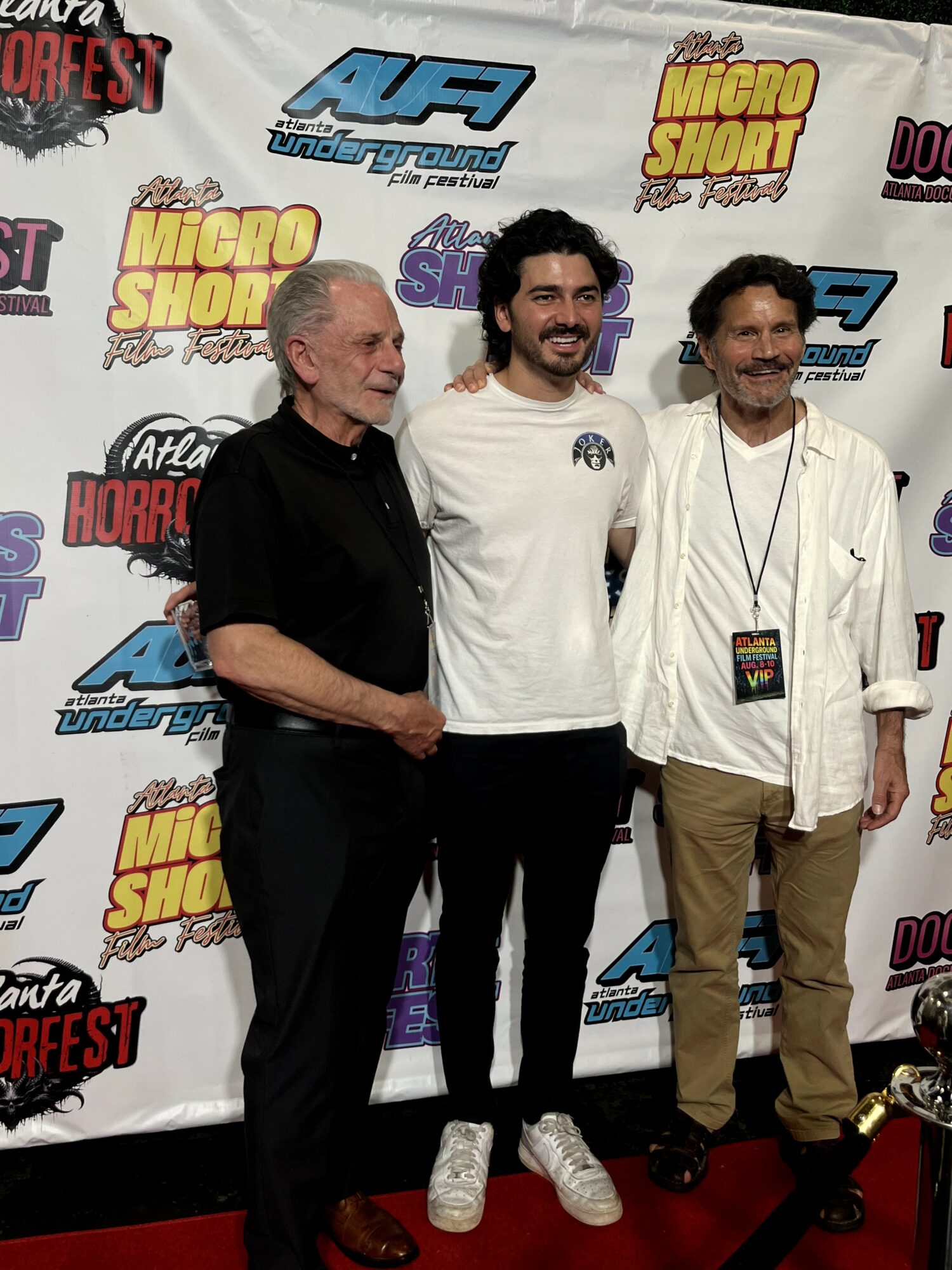 Three men standing in front of a backdrop with various logos, smiling and posing for the photo.