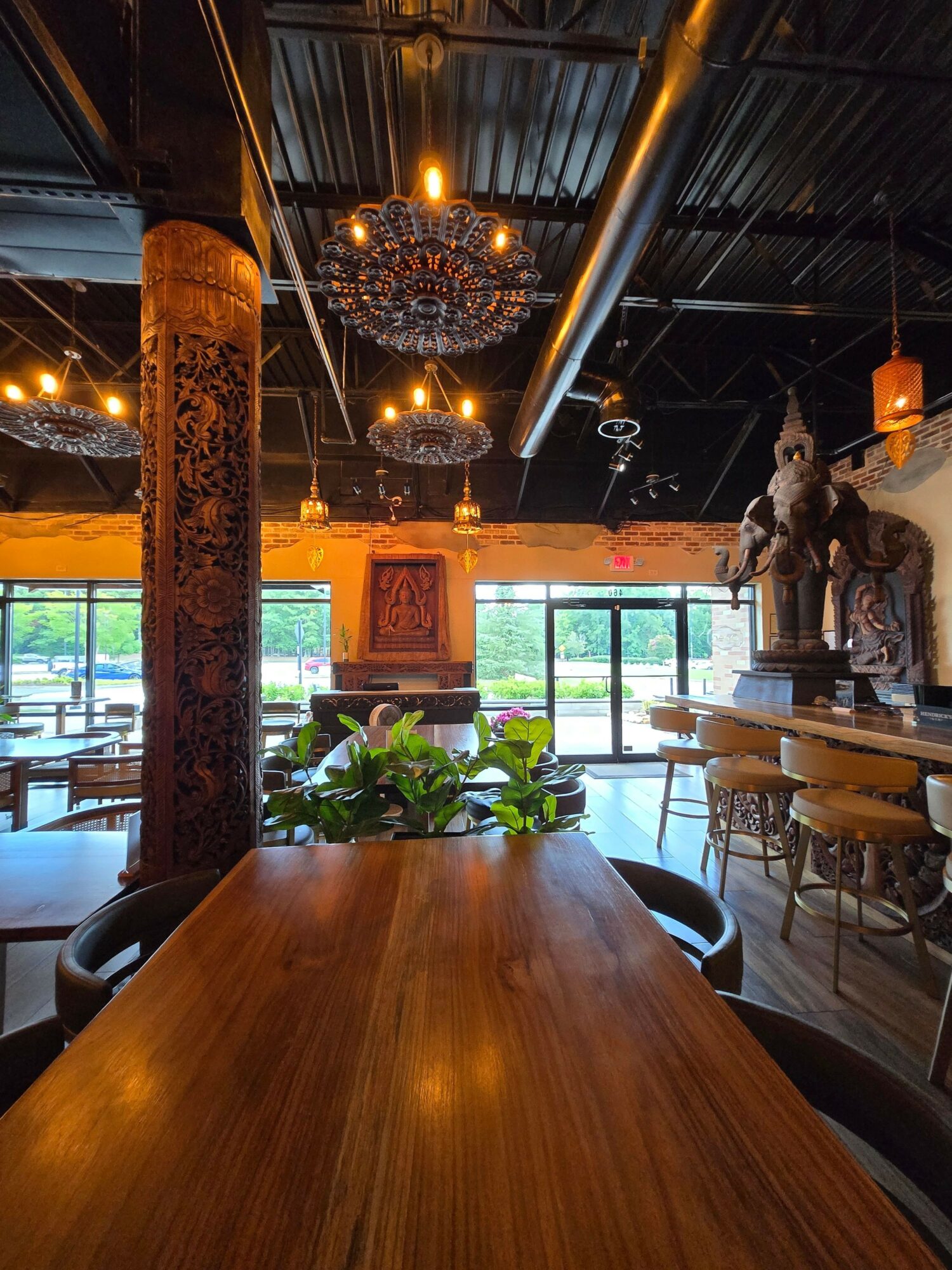 Interior of a cafe with wooden tables, plants, and hanging lights, viewed from a table's edge.