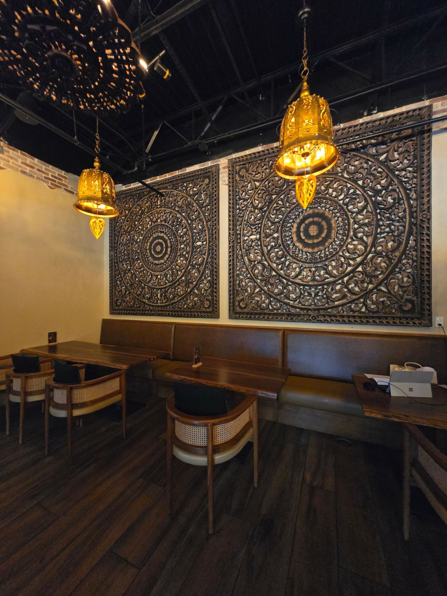Decorative wall with intricate patterns, hanging golden lamps, and a wooden table with chairs in a dimly lit room.