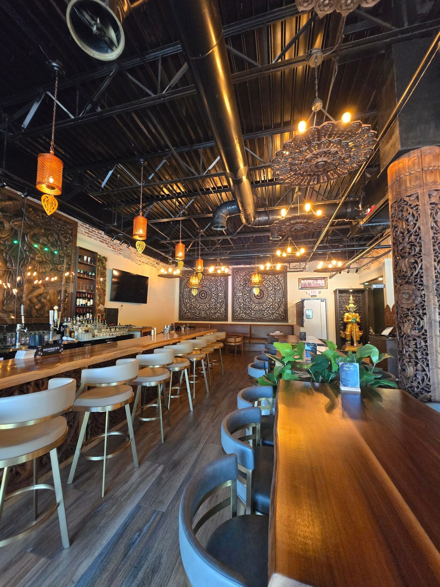 Interior of a restaurant with hanging lights, a bar area, and a row of chairs along a wooden counter.