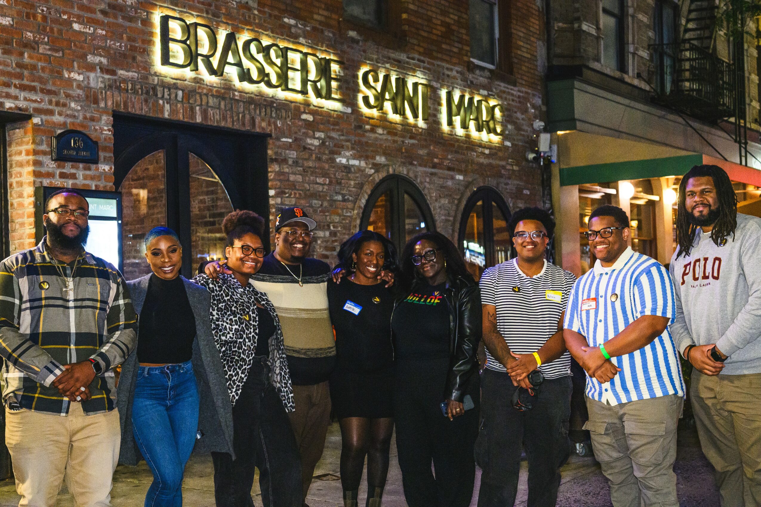 Group of people standing outside a brick building with a sign reading 'Brasserie Saint-Michel'.