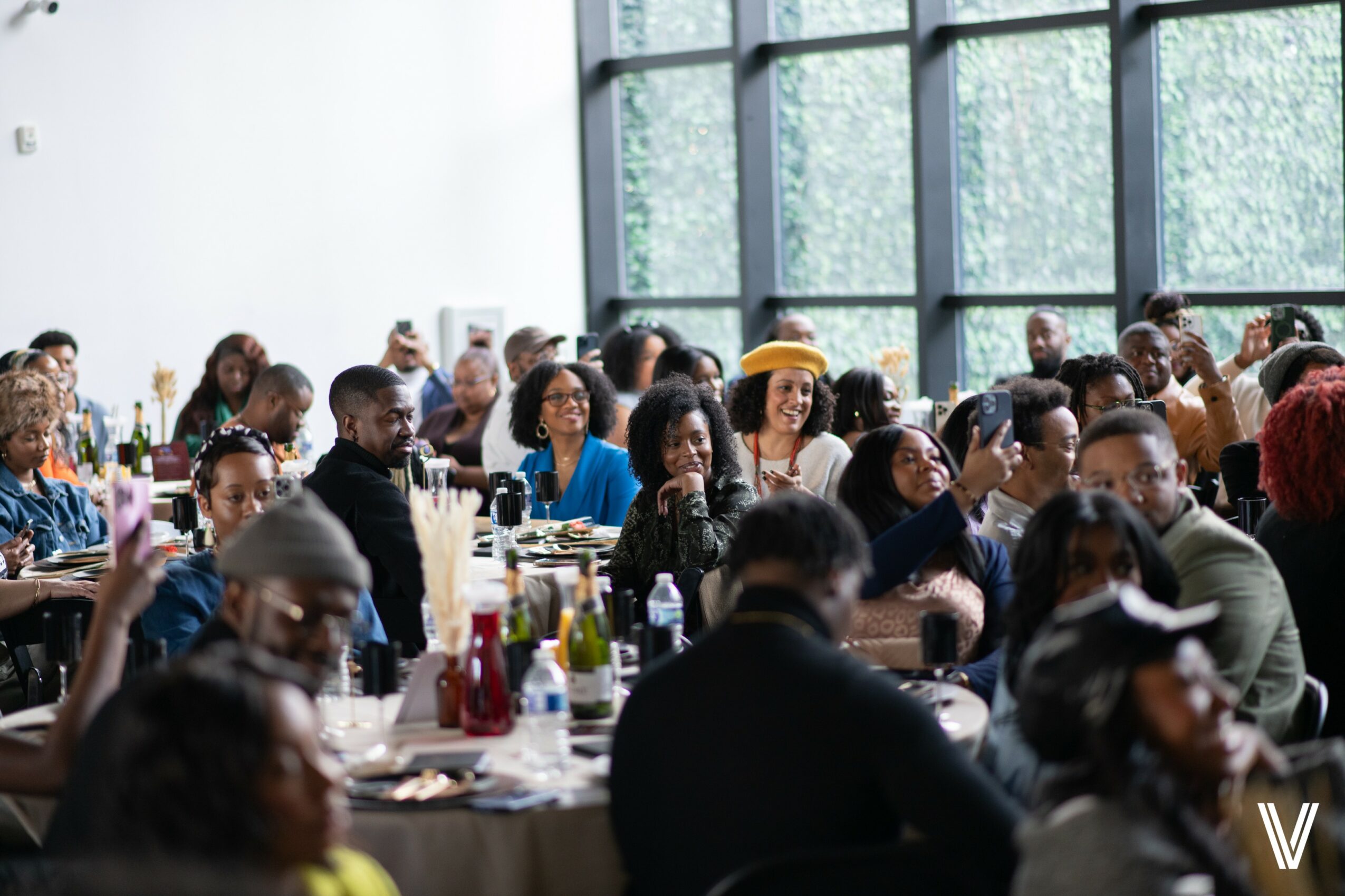 People seated at tables in a bright, modern room with large windows, engaging in conversation and dining.
