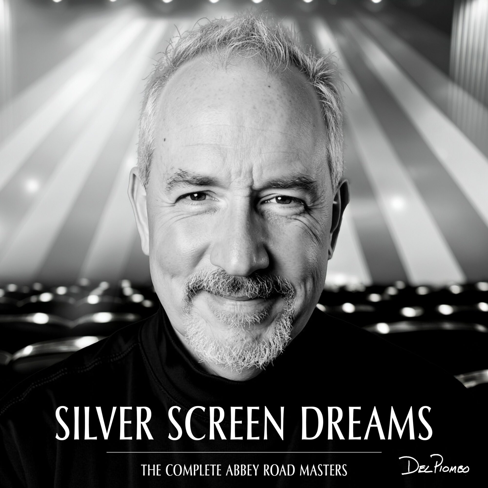 Black and white portrait of a smiling man with a background of stage lights and empty seats.