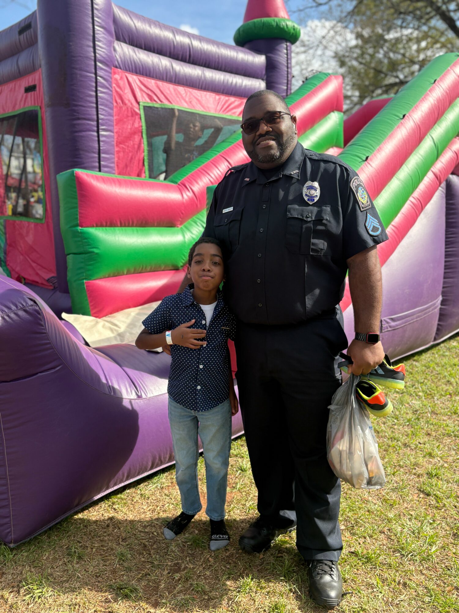 A police officer and a young girl stand together outdoors in front of a colorful inflatable slide, smiling at the camera.