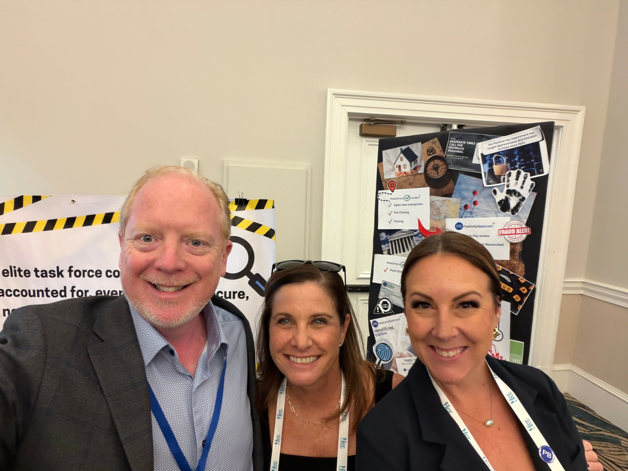 Three people smiling in front of a bulletin board with various flyers and notices, indoors.
