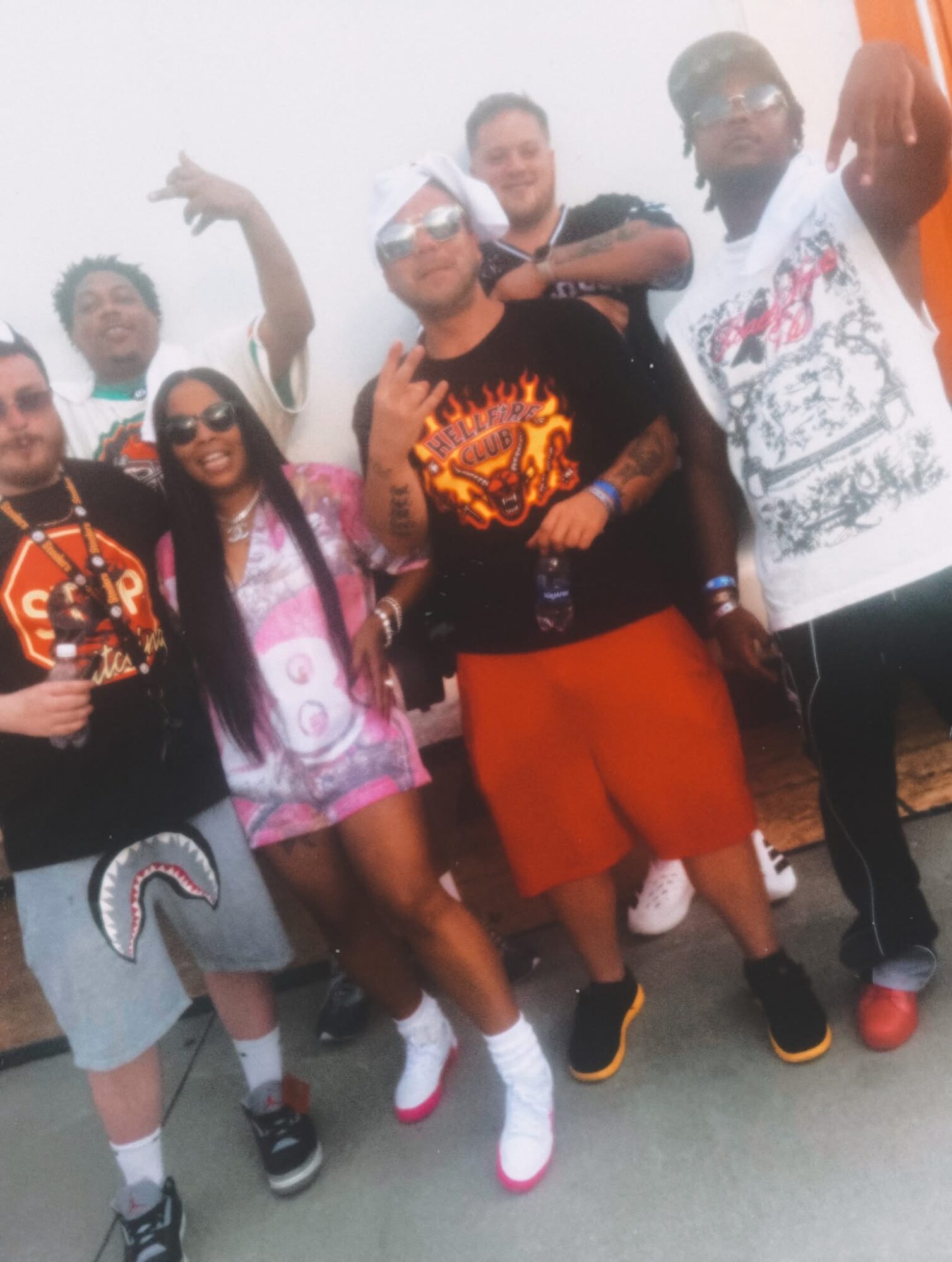 Group of six people posing outdoors, some making gestures, wearing casual and colorful clothing.