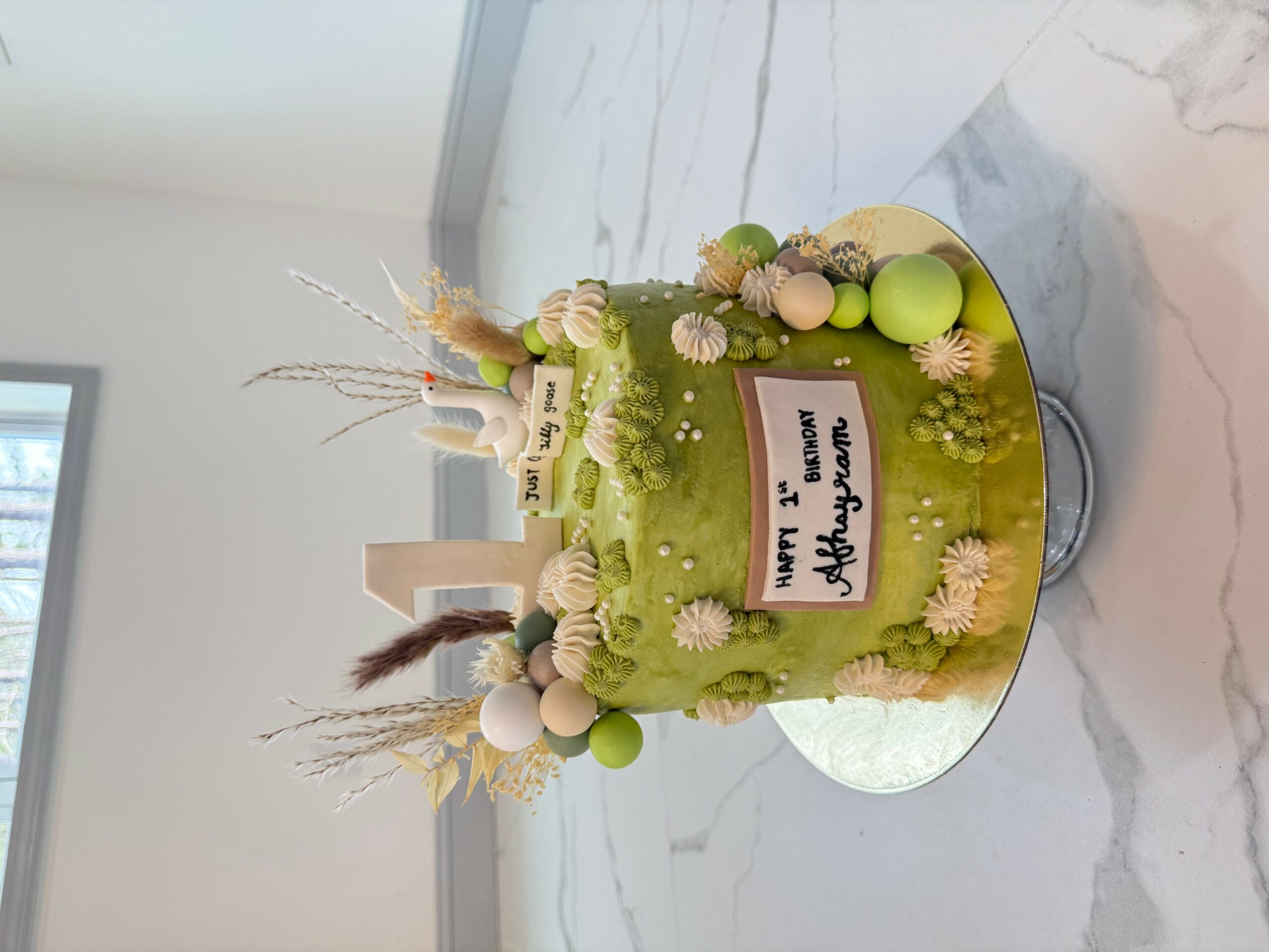 Green birthday cake decorated with flowers, balls, and a message on top, placed on a marble surface.