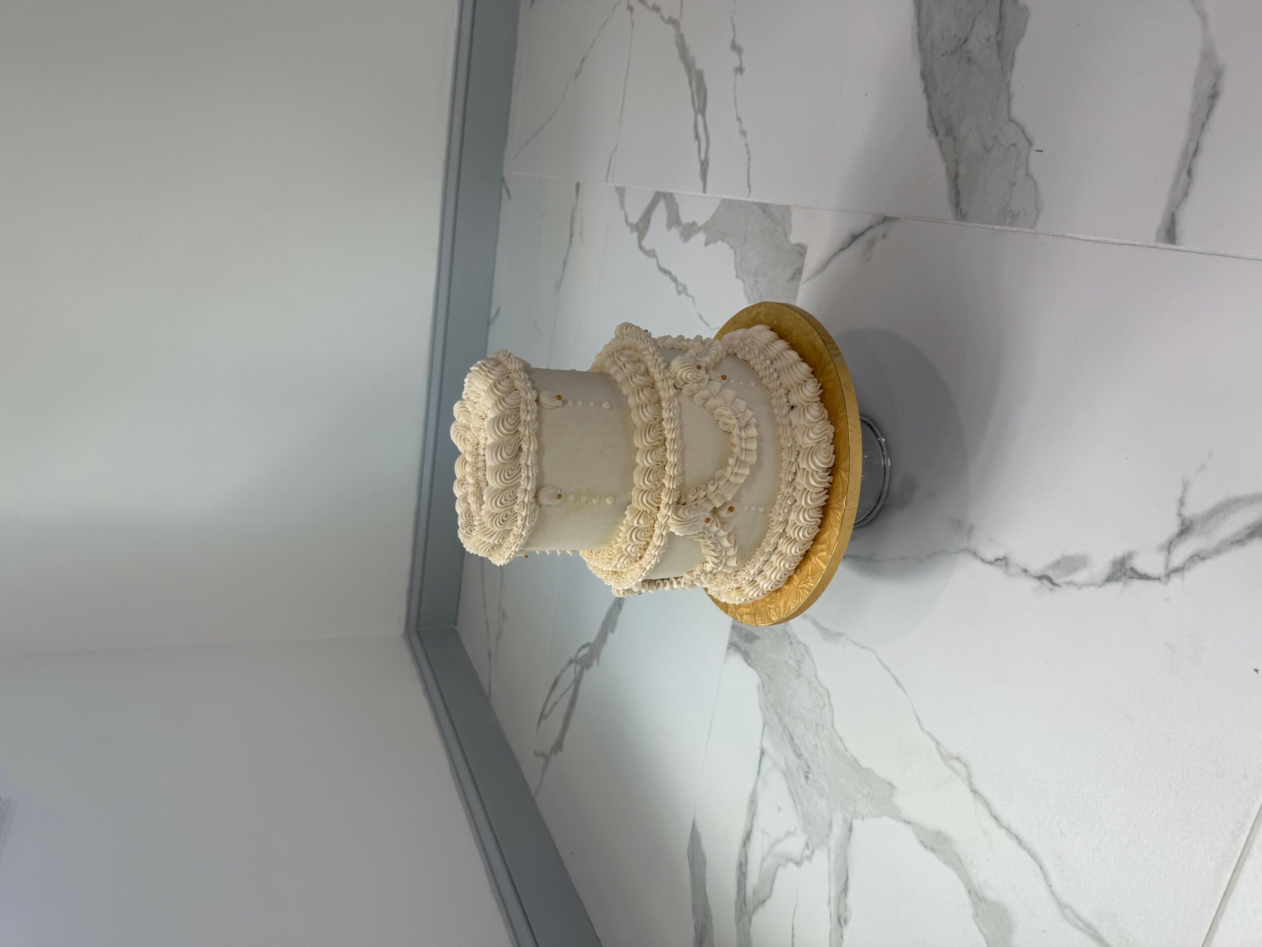 Three-tiered white cake with decorative icing, on a marble surface, with a plain background.