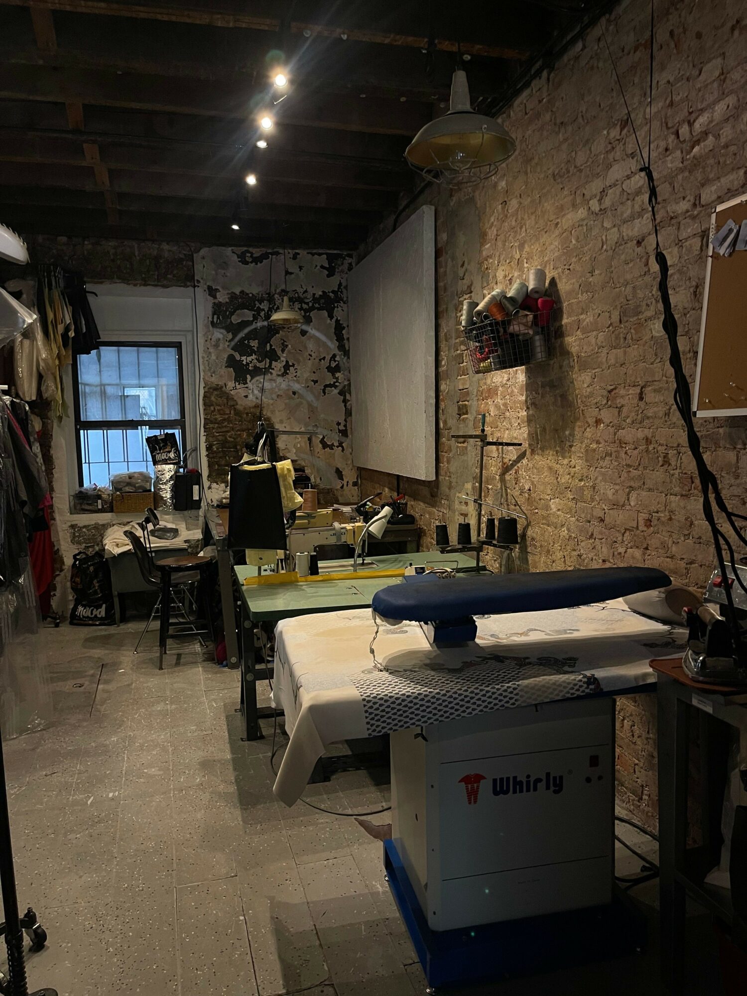 Workshop with table, equipment, and tools, brick wall, window, and various objects on the table.