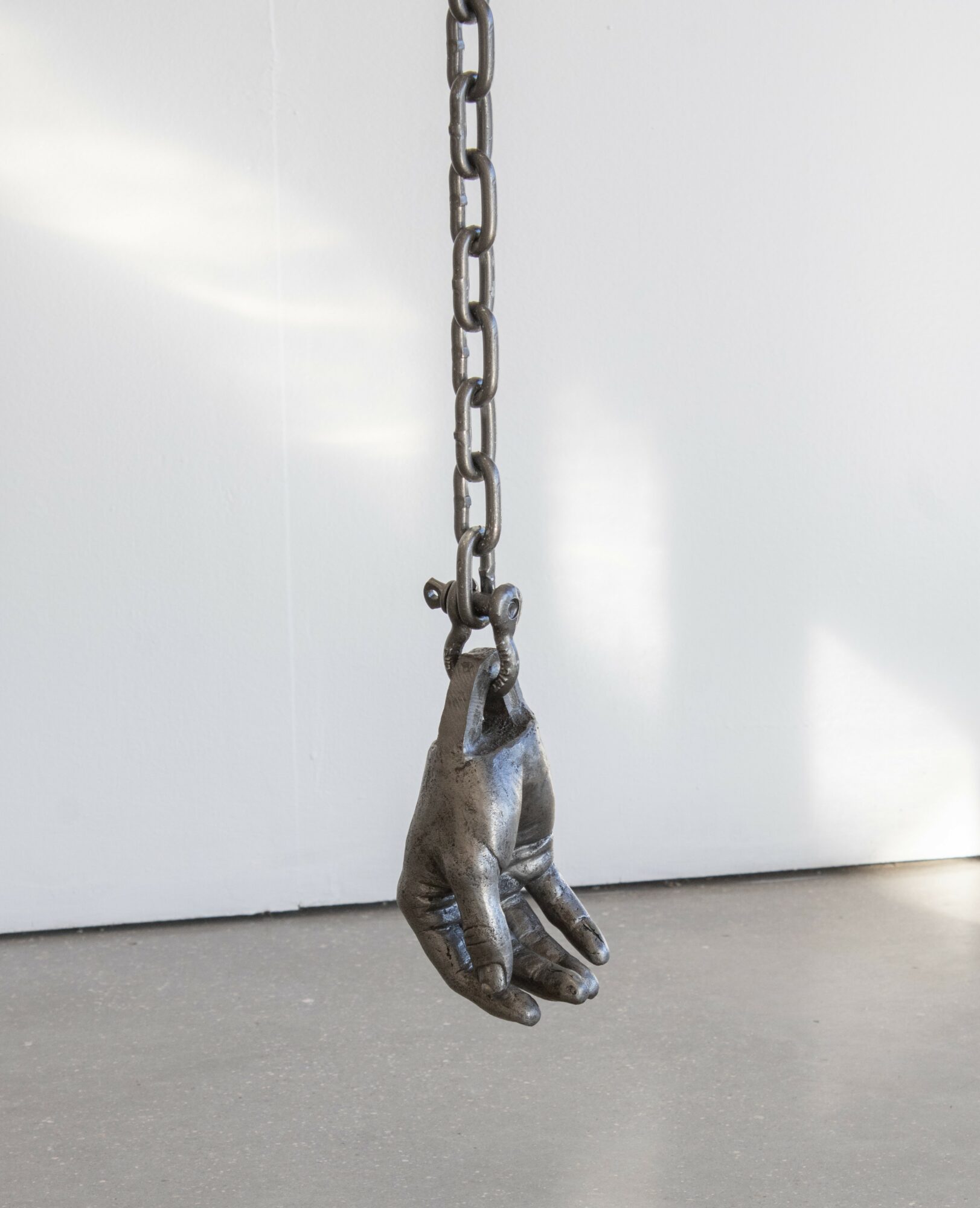 A metal sculpture of a hand hanging from a chain against a white background.