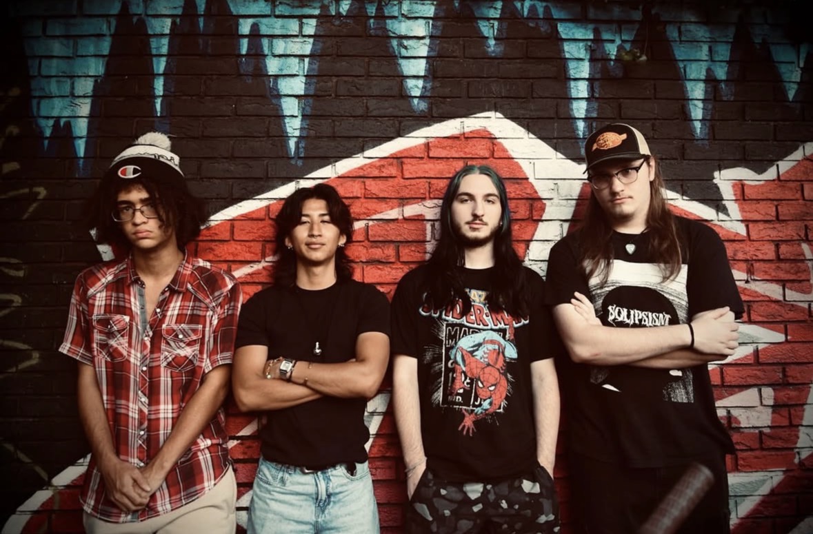 Four young people stand in front of a colorful graffiti wall, posing with arms crossed or relaxed. 20 words.