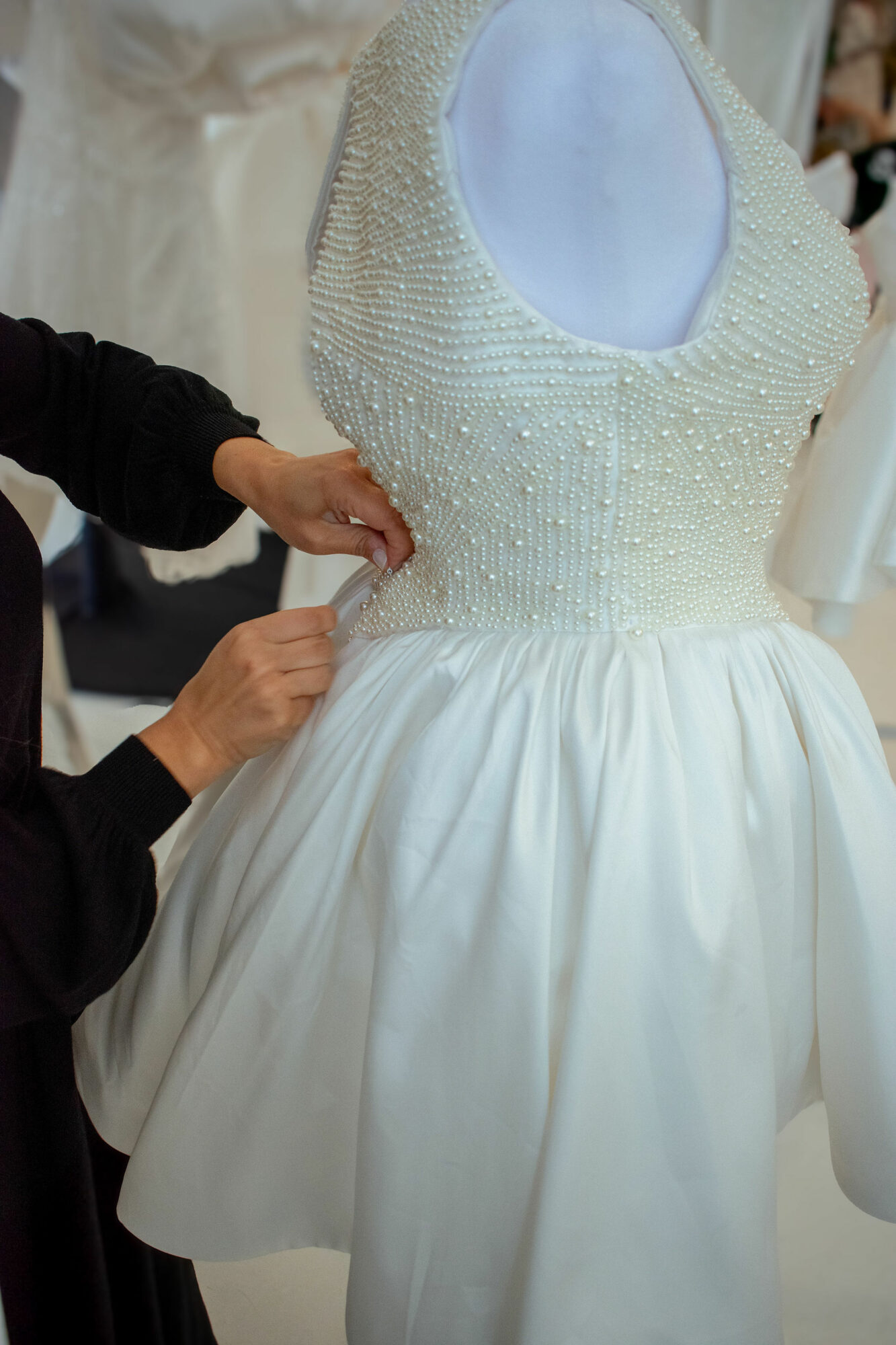 Person adjusting a white dress with a beaded bodice and full skirt, mannequin visible in the background.