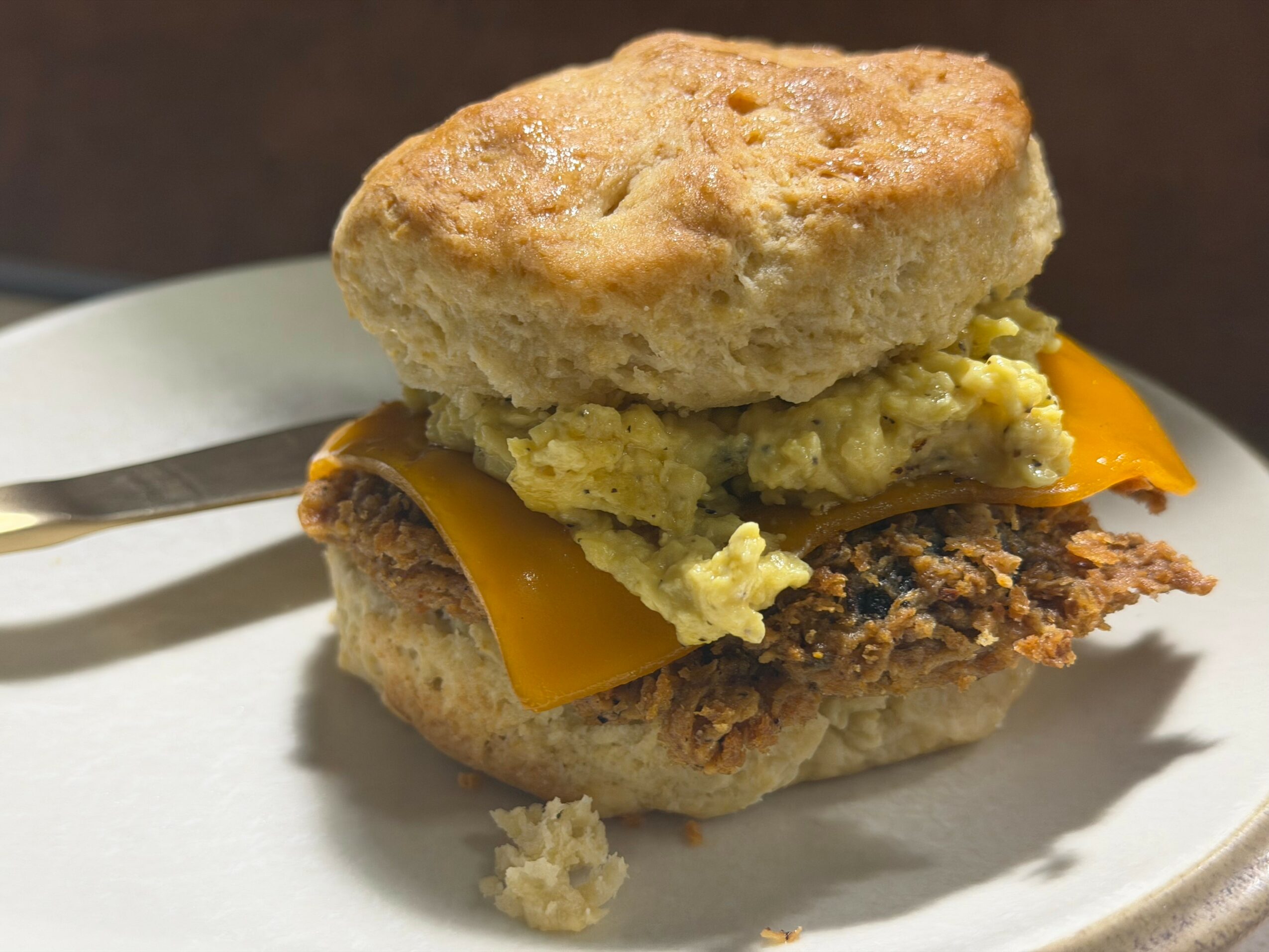Scone with egg, cheese, and fried chicken on a plate, with a knife nearby