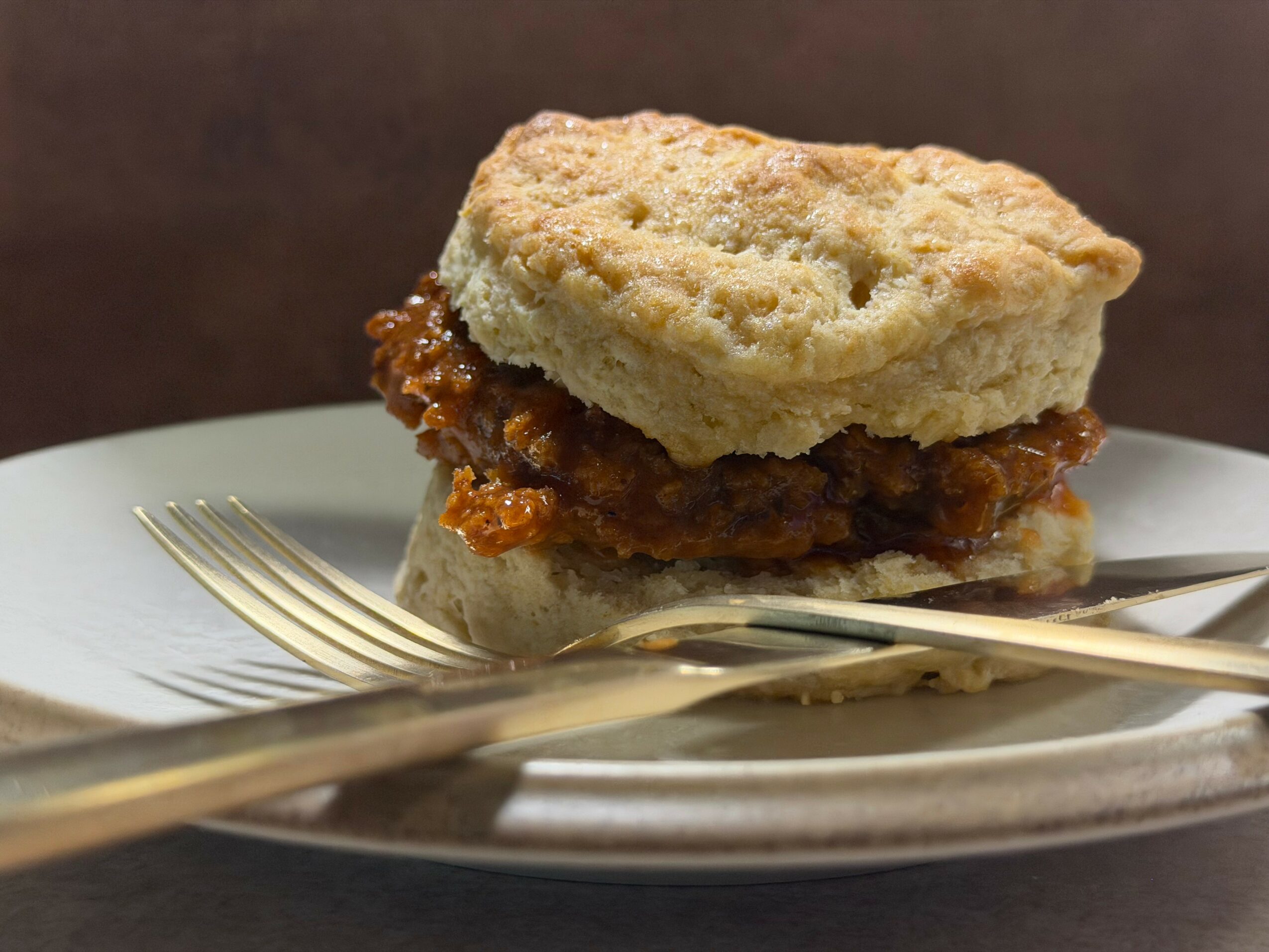 Fried chicken sandwich with biscuit bun on a plate, with a fork and knife, close-up view.