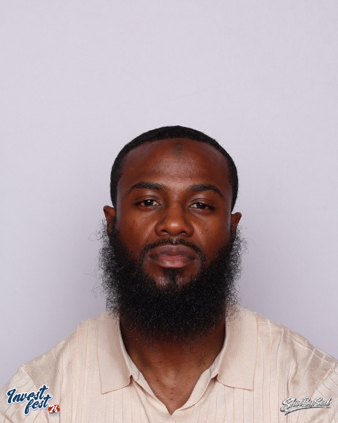 Portrait of a man with a beard and short hair, wearing a light-colored shirt, against a plain background.