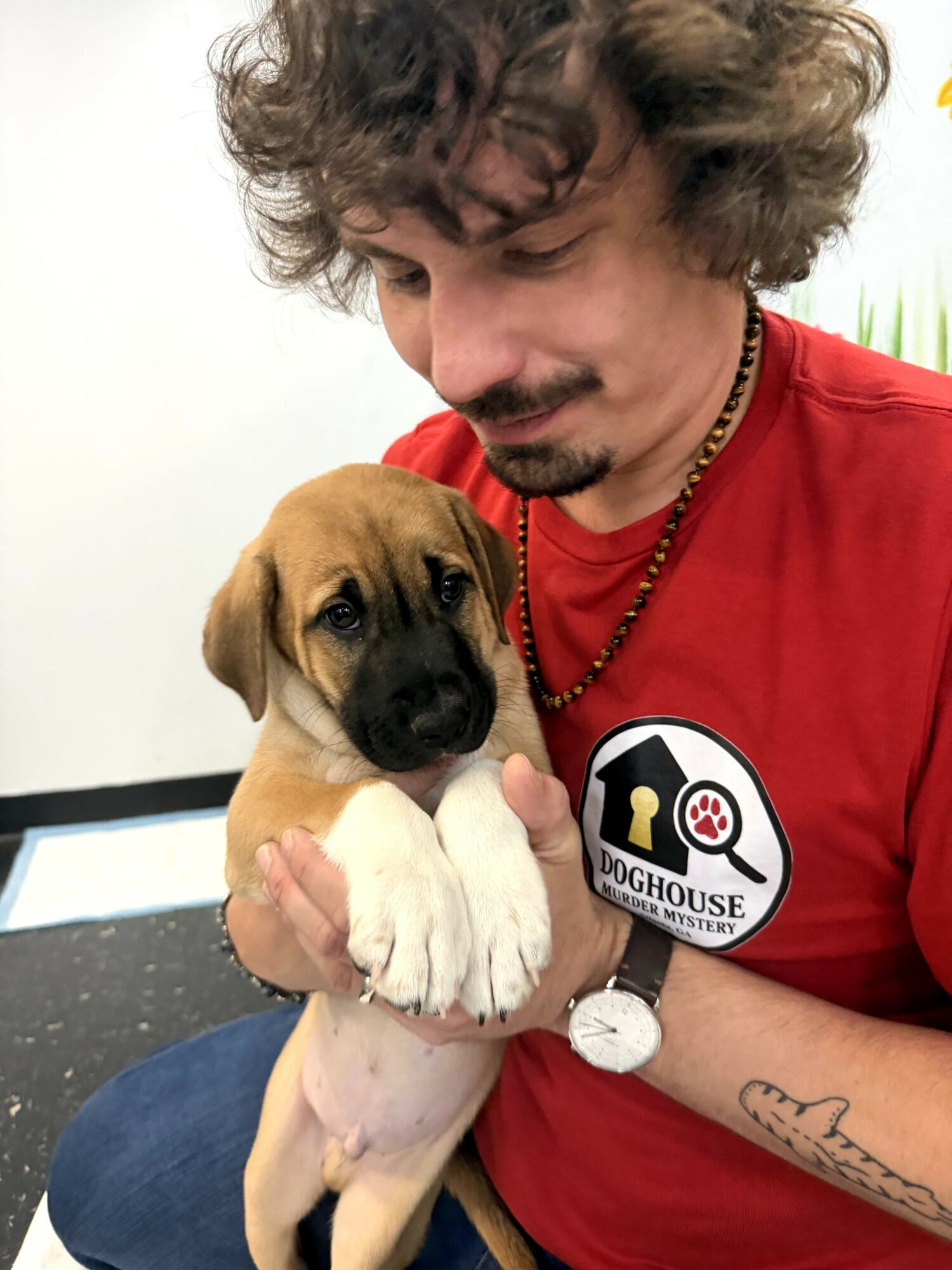 Man holding a puppy with a red shirt and a logo, looking at the puppy affectionately.