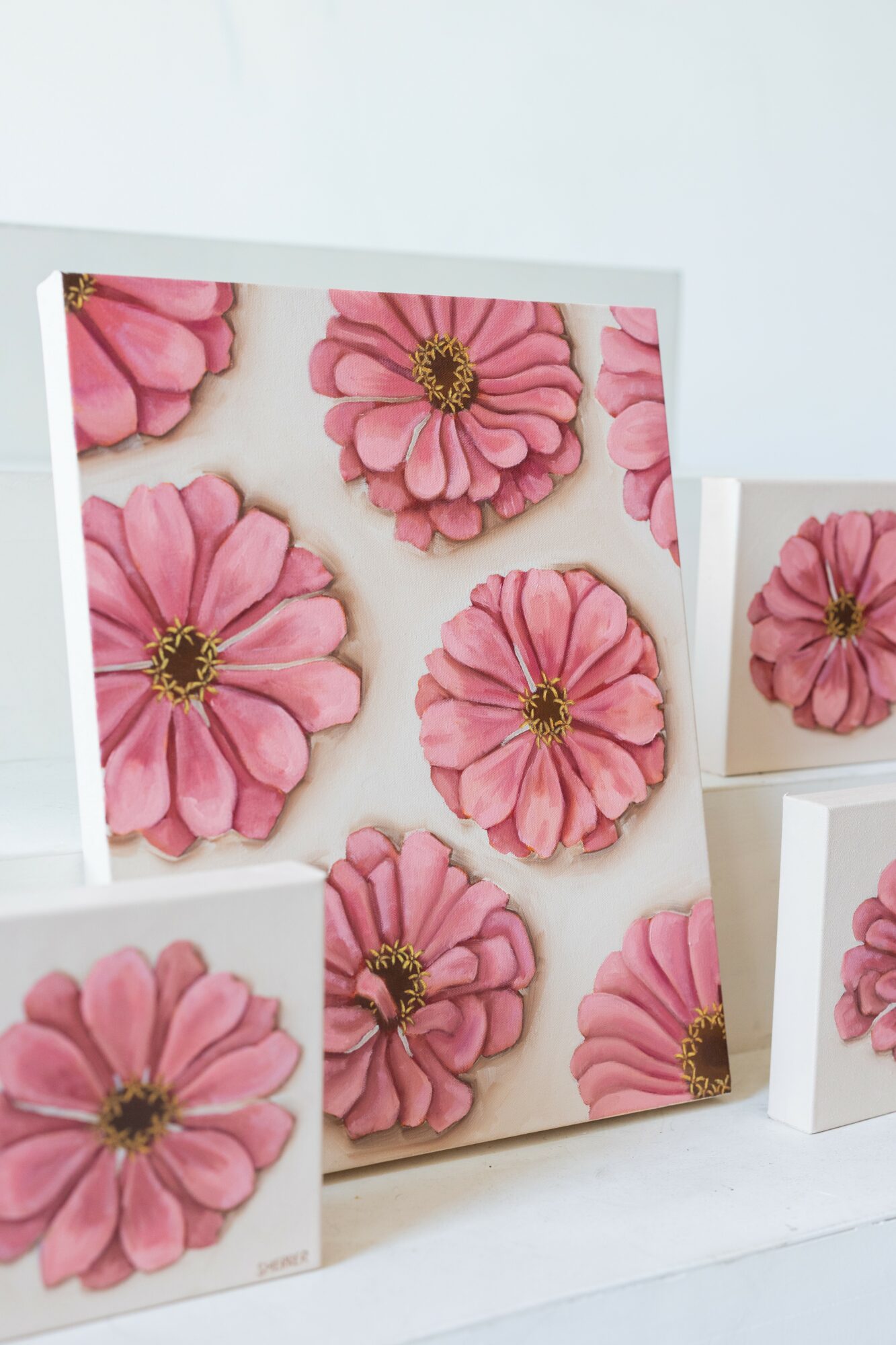 Square canvas with pink flowers and yellow centers, surrounded by smaller similar canvases, all with white backgrounds.