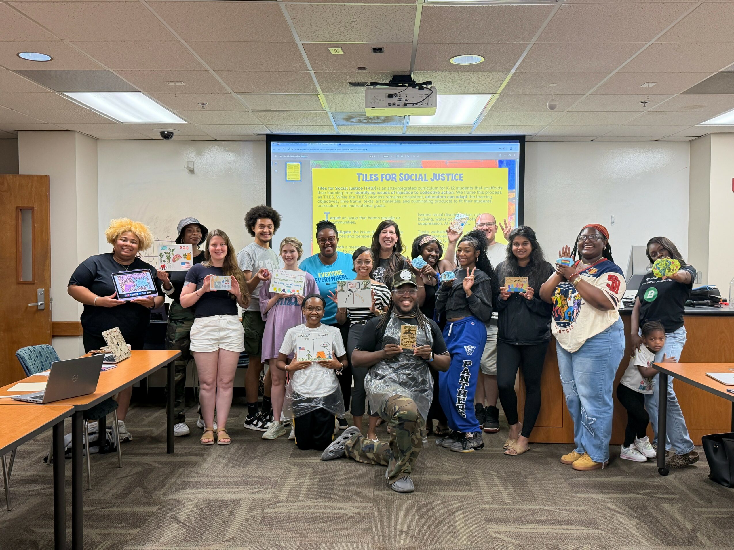 Group of diverse people in a classroom, some holding certificates, with a presentation screen behind them.
