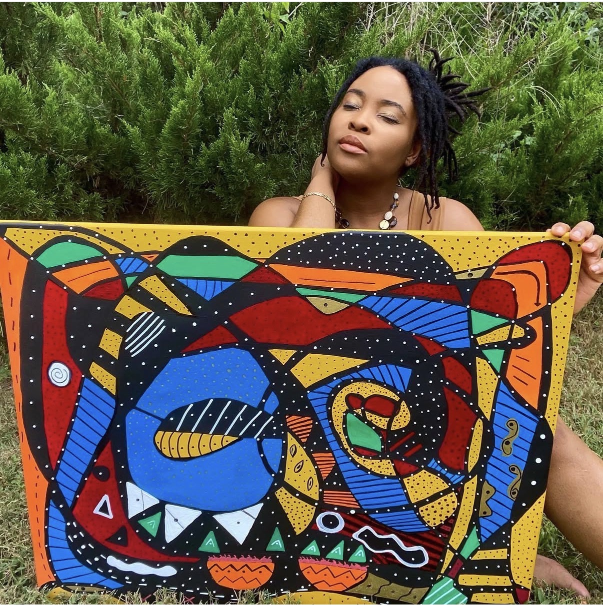 Woman with closed eyes holding a colorful, abstract painting outdoors, surrounded by green foliage.