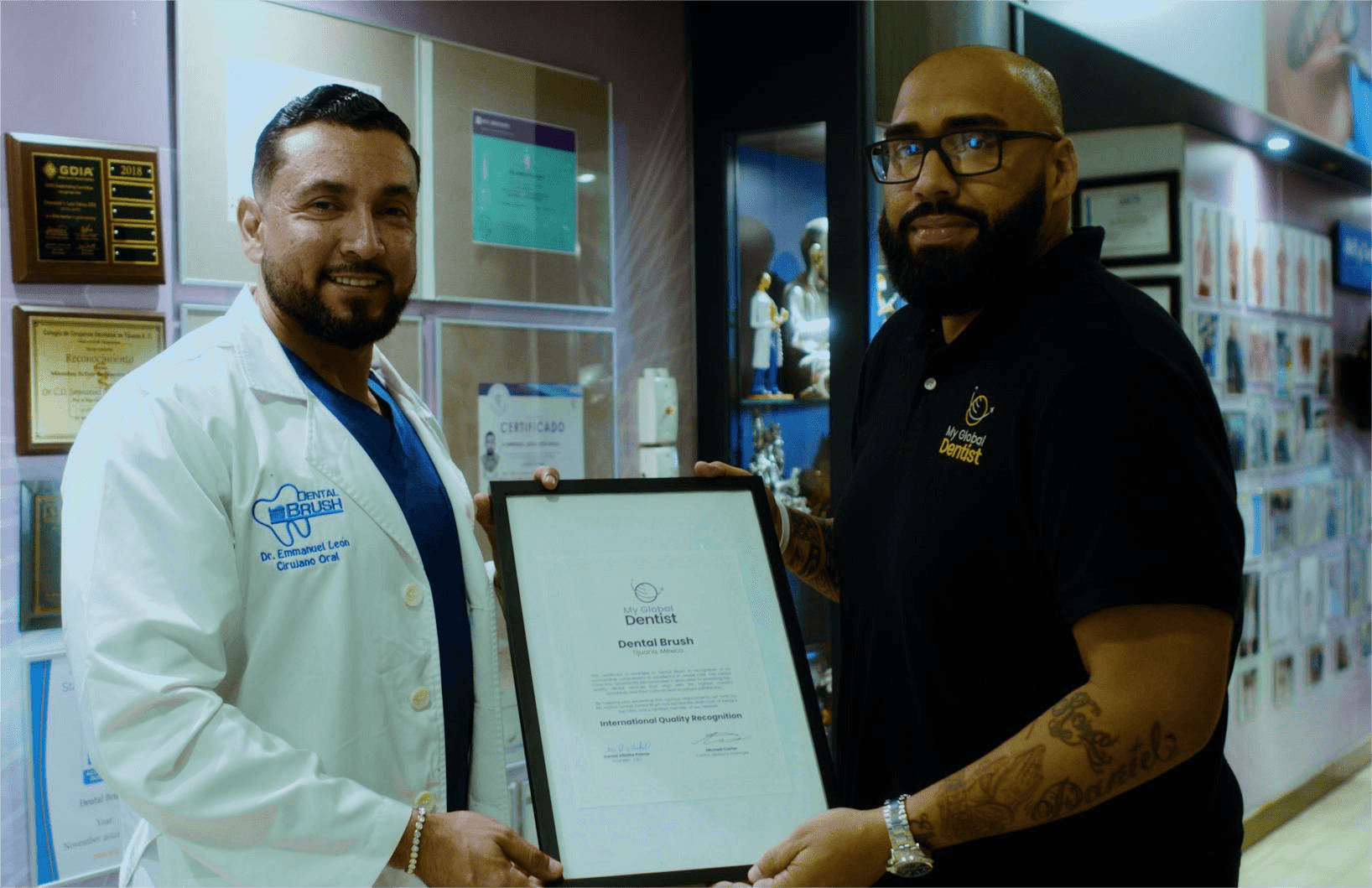Two men, one in a white coat and the other in black, hold a framed certificate in a store or clinic.