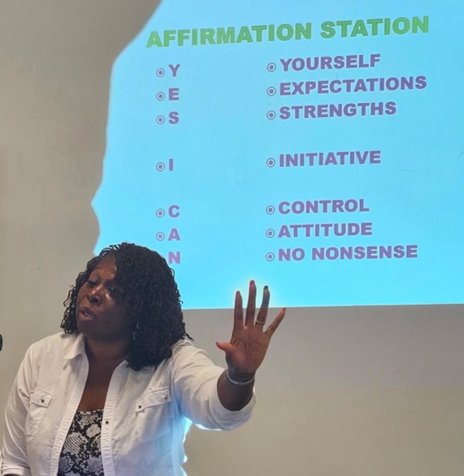 Woman presenting in front of a slide titled 'Affirmation Station' with bullet points and text.