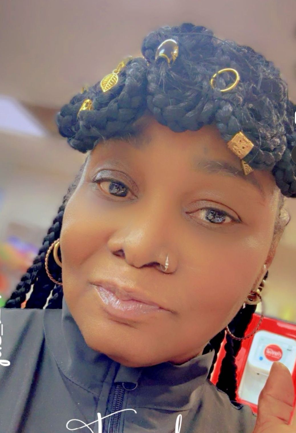 Person with styled hair, nose ring, earrings, and a black top, holding a phone with a red and white screen.
