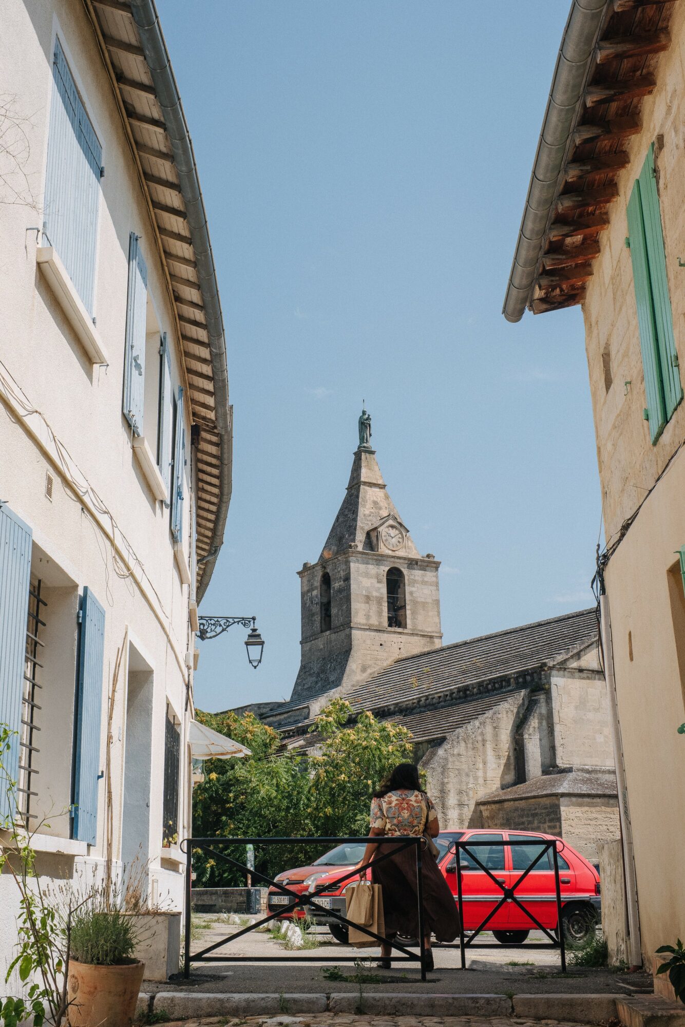 Person sitting on a bench in a narrow street with colorful buildings and a church tower in the background.