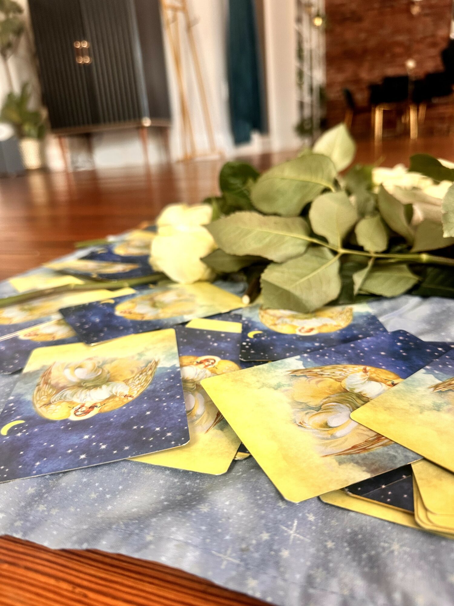 Cards spread on a table with a bouquet of white roses in the background, in a room with wooden floors and curtains.