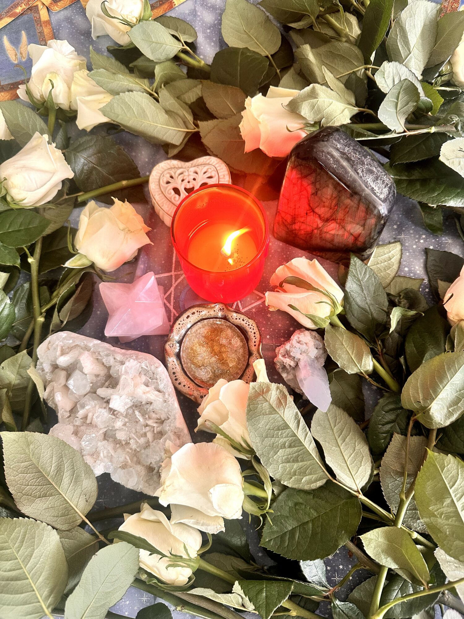 Flowers, candles, and decorative objects arranged with greenery and roses, creating a romantic or memorial setting.