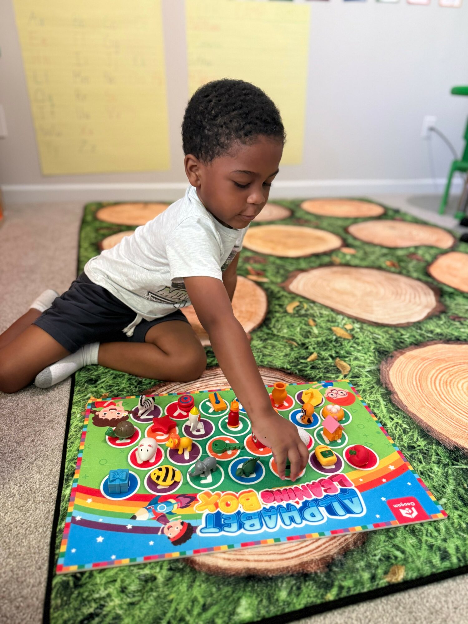 Child playing a colorful board game on a green surface with wooden tree slices in the background.