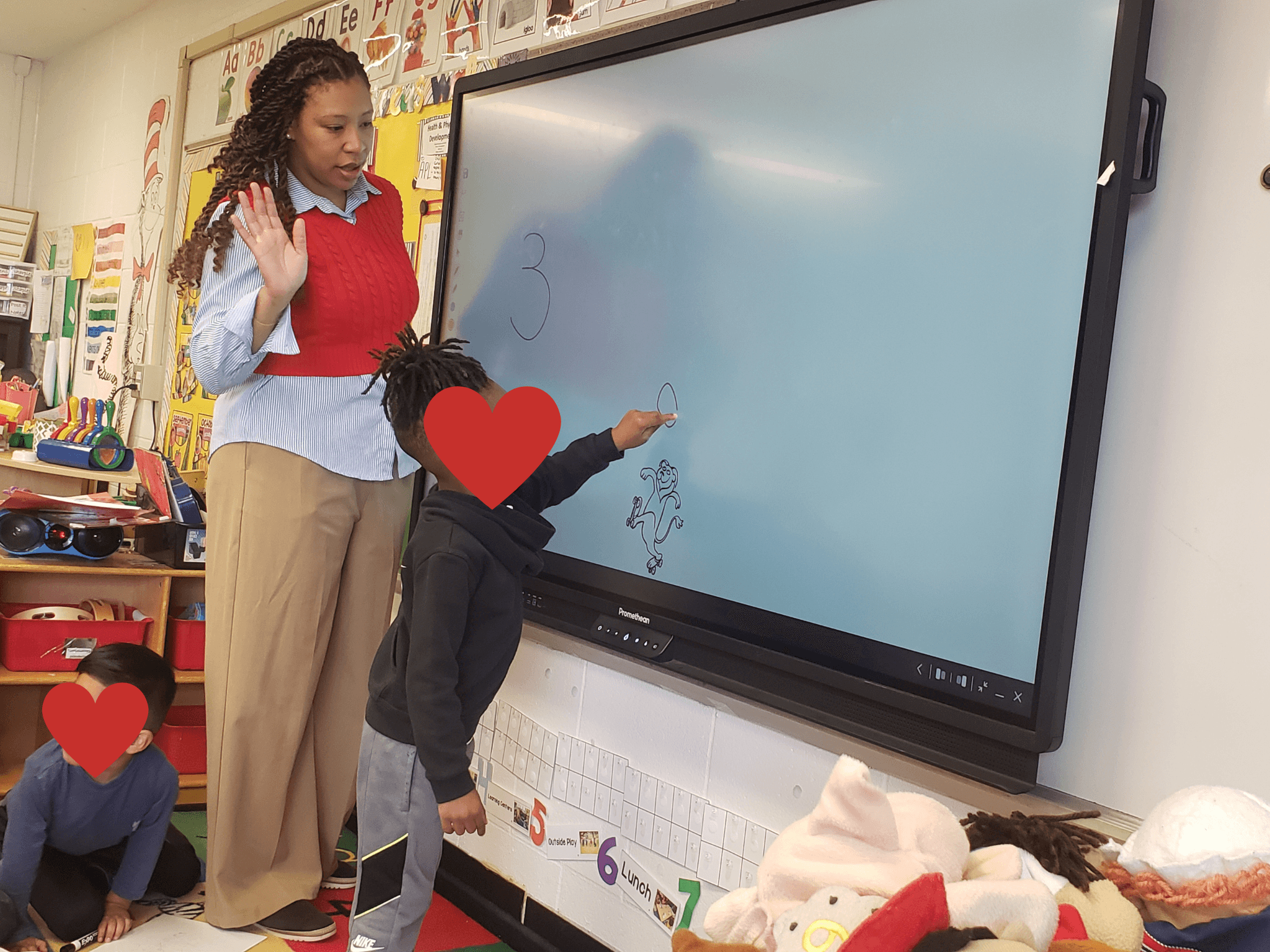 Child writing on a large interactive whiteboard with a teacher observing in a classroom.