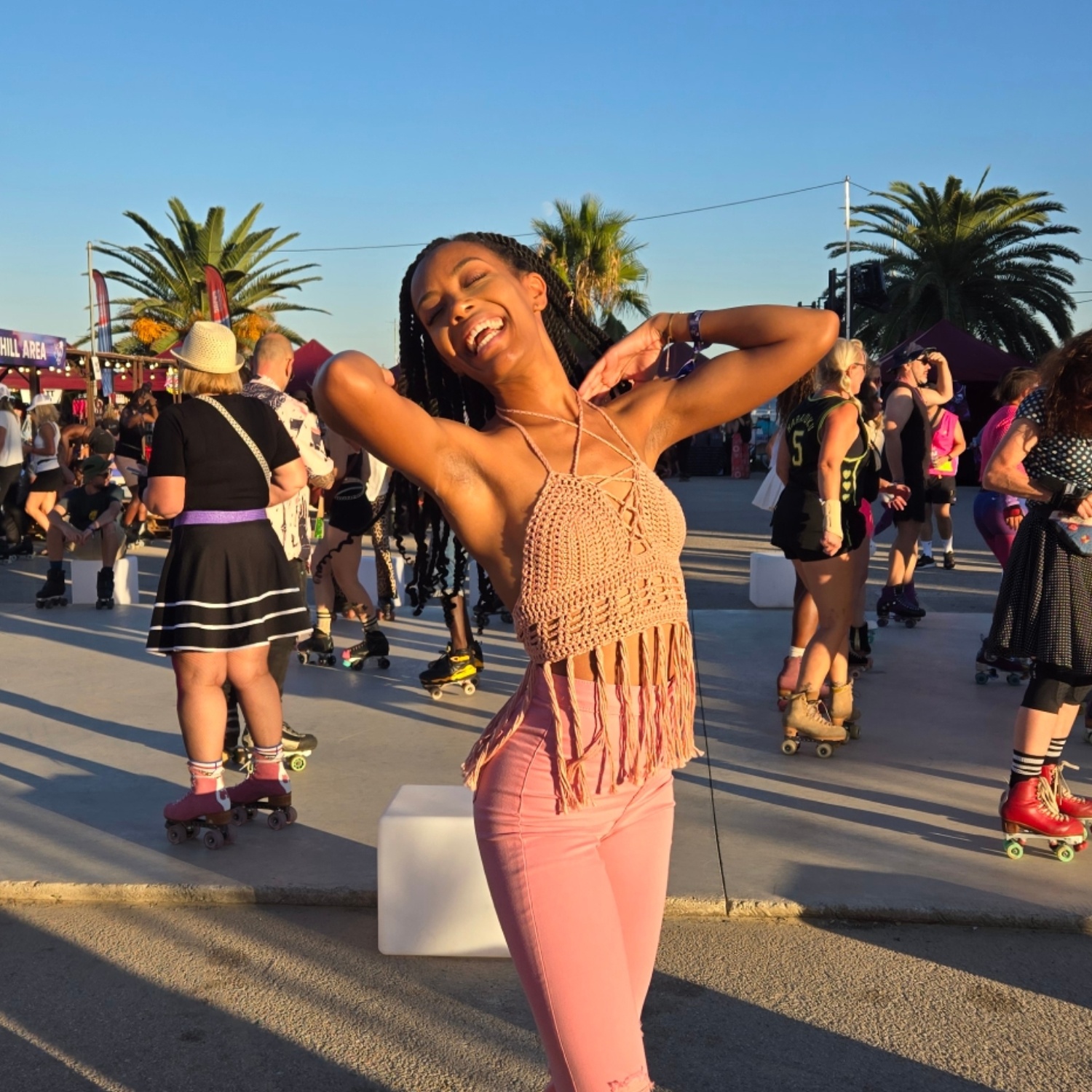 Woman smiling and dancing outdoors with people and palm trees in the background.