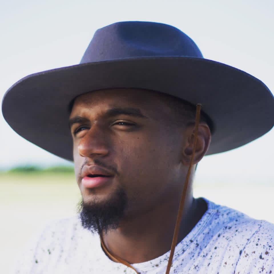 Man wearing a wide-brimmed hat outdoors, looking to the side, with a blurred background.