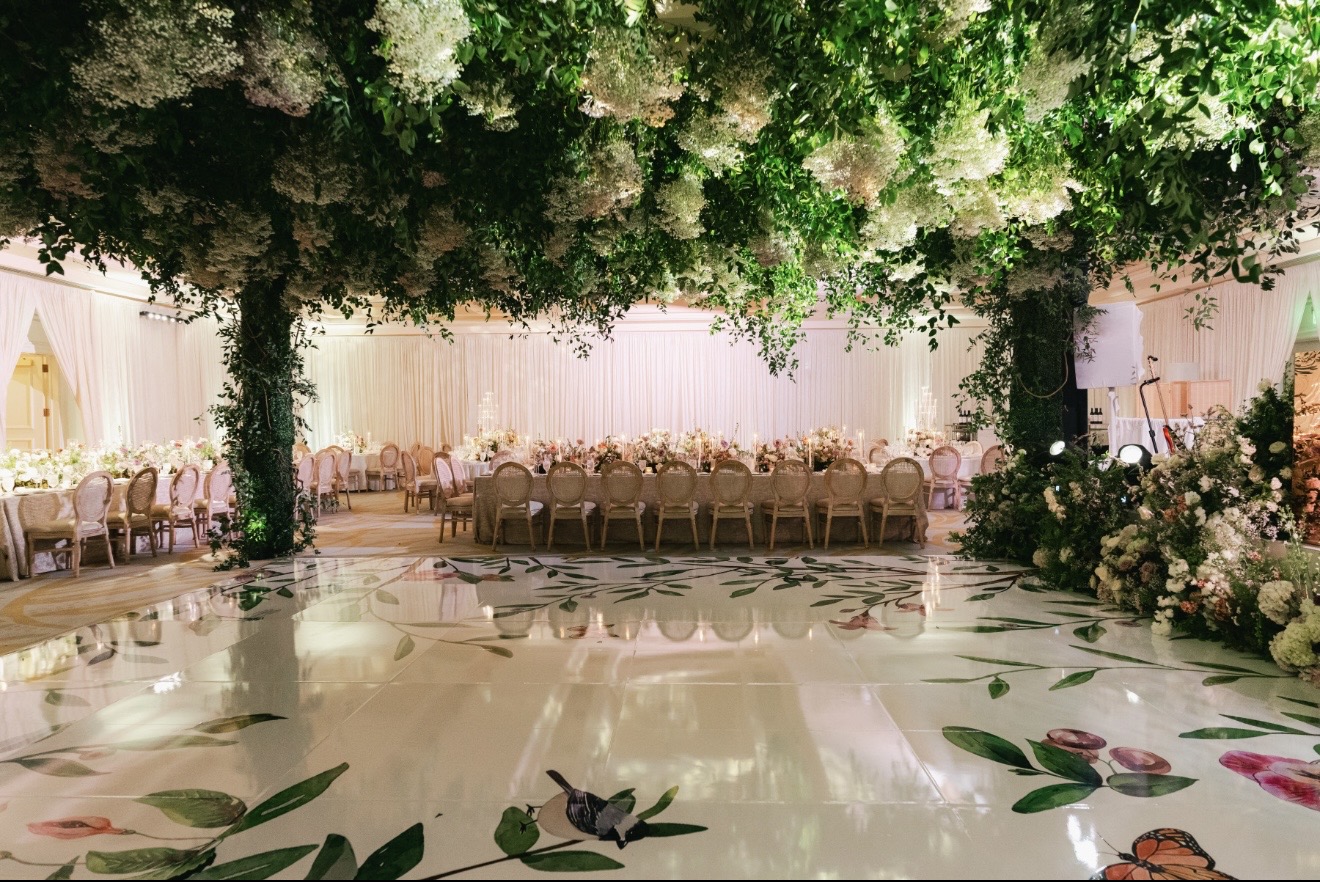 Elegant event space with floral ceiling, long table, and decorated dance floor with leaf and butterfly designs.