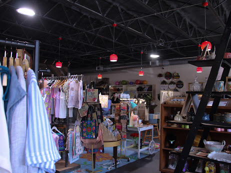 Clothing store interior with racks of clothes, shelves, and display tables, under a black ceiling with red lights.