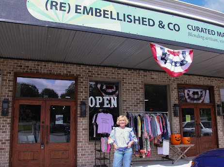 Person standing outside a store with clothing and Halloween decorations, including a pumpkin, in front of brick walls and glass doors.