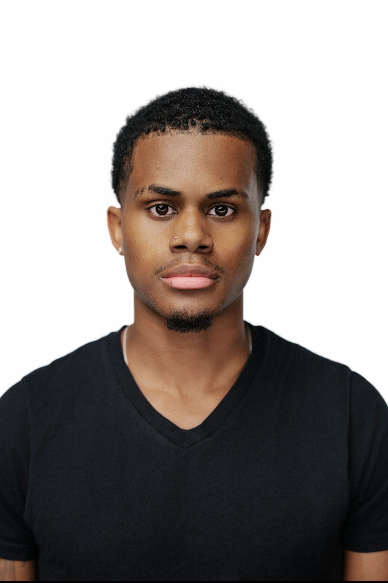 Young man with short curly hair and a serious expression, wearing a black V-neck shirt, facing forward.