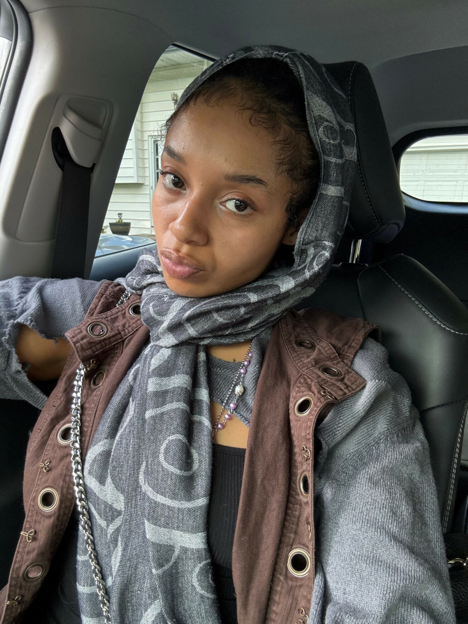 Child with hoodie and jacket sitting in car seat, looking at camera, inside vehicle interior.