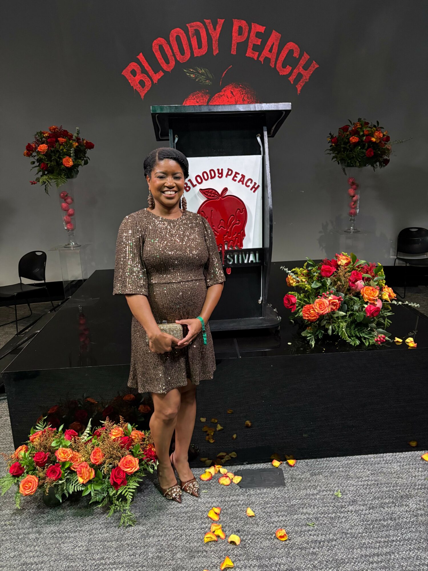 Person in a sparkly dress standing on stage with flowers and a sign reading 'Proud to Pack' behind them.