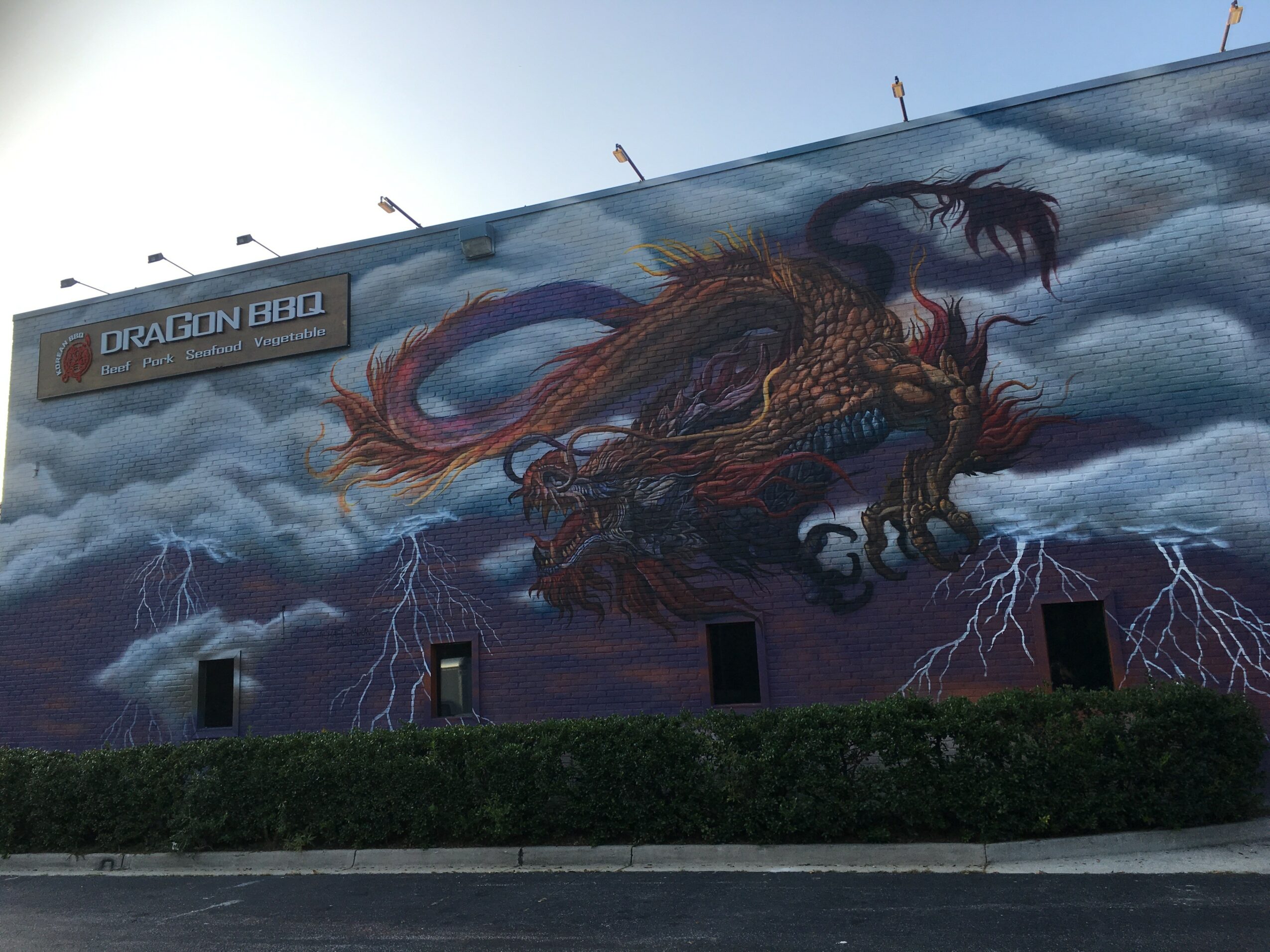 Large mural of a dragon with wings, surrounded by storm clouds and lightning, on a building wall.