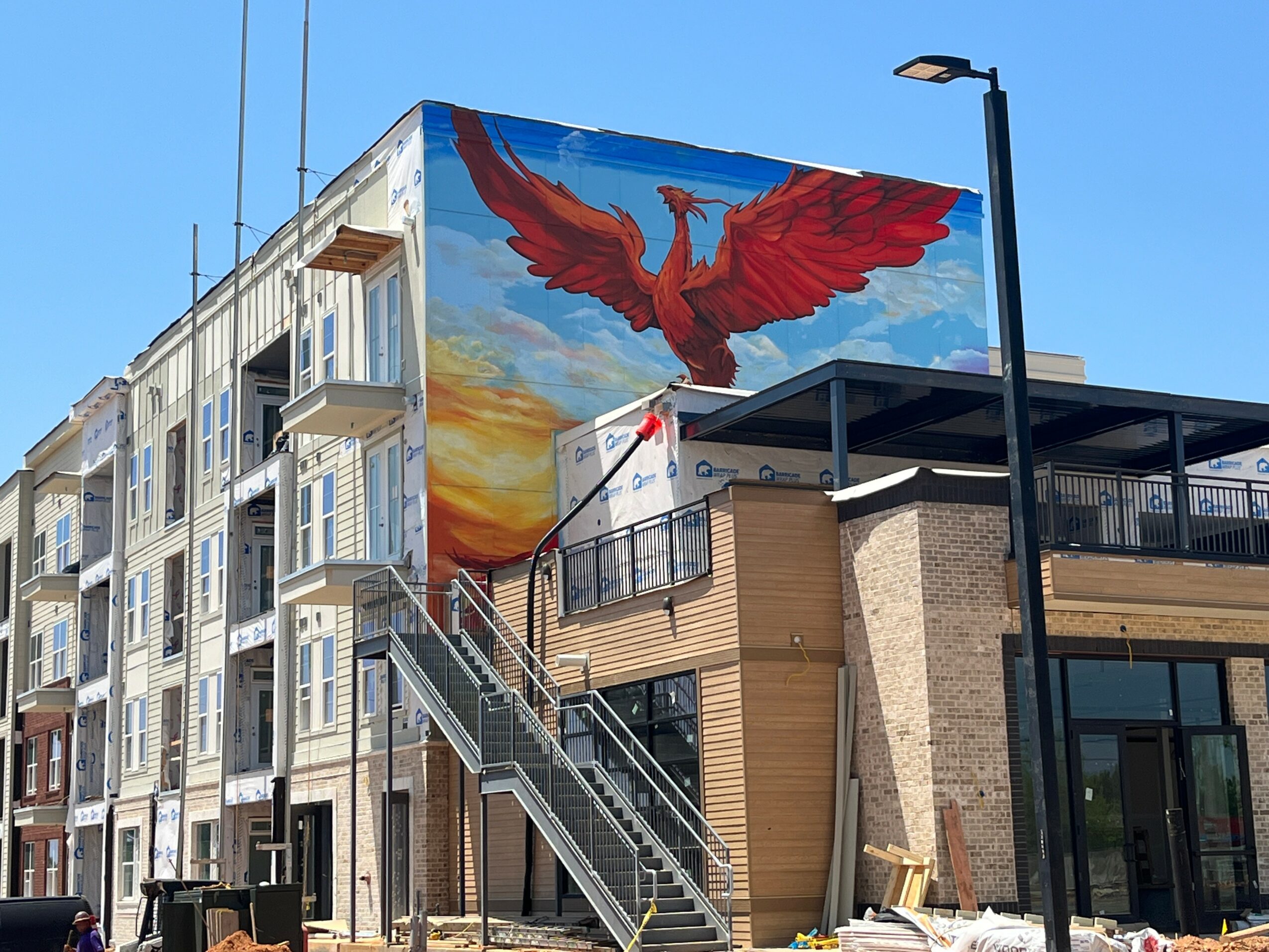 Building with a large mural of a red bird flying against a colorful sky, stairs, and a streetlamp.